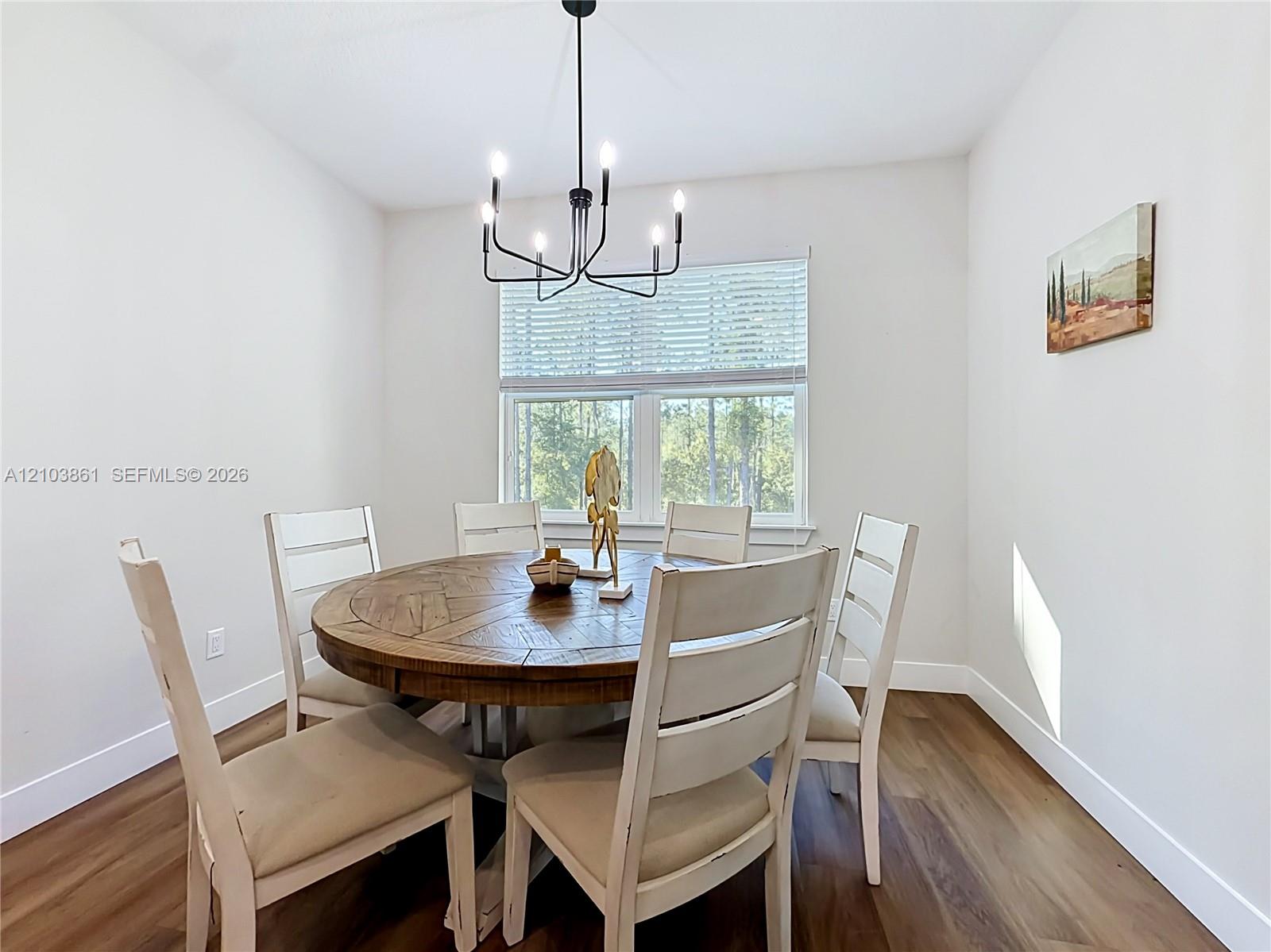 Dining area featuring wood-finish flooring, a matte black multi-arm chandelier, and a window with horizontal blinds