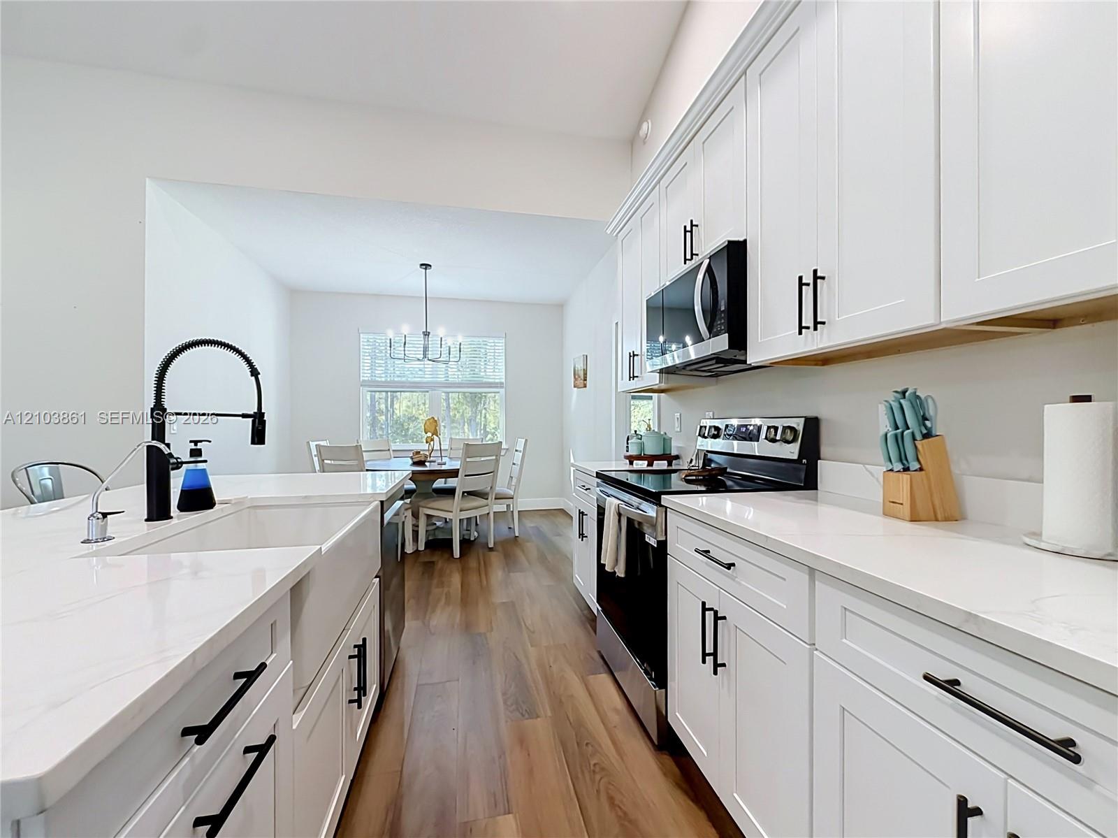 Kitchen featuring white shaker-style cabinetry, quartz countertops, a farmhouse-style apron sink with a matte black faucet, and wood-finish flooring