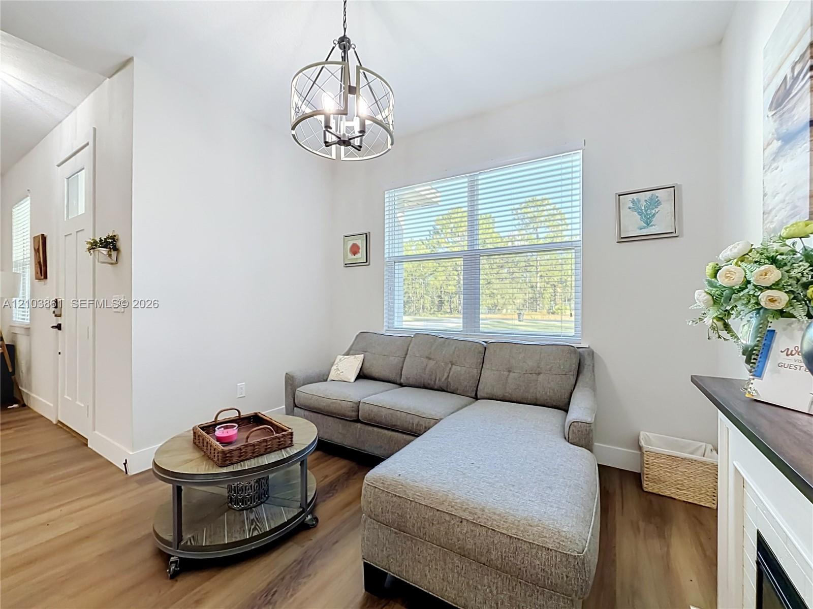 Wood-finish flooring, industrial-style circular chandelier, large window with blinds, and white panel door