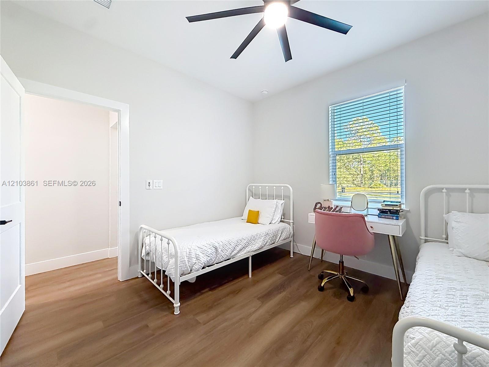 Room featuring wood-finish flooring, a matte black multi-blade ceiling fan, and a single-hung window with integrated horizontal blinds