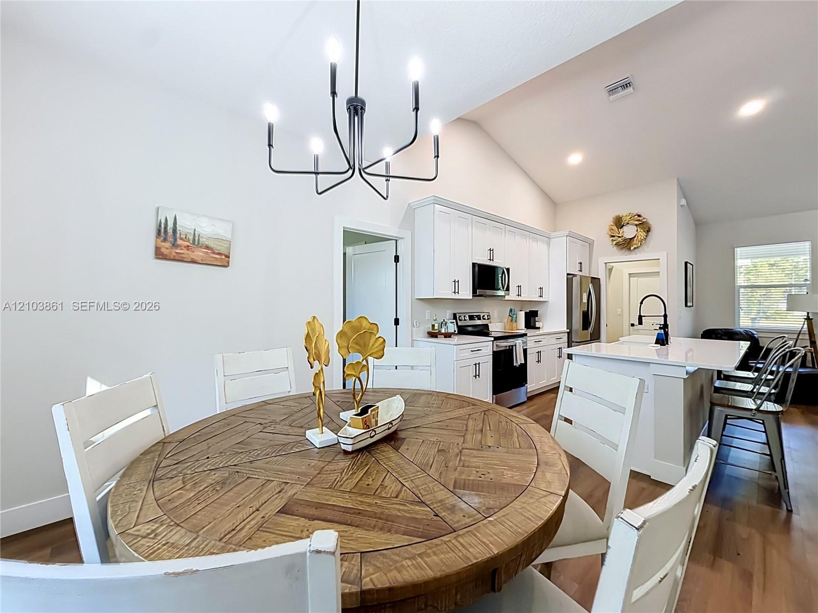 Open-concept kitchen featuring white shaker cabinetry, stainless steel appliances, a central island with a solid-surface countertop, and a contemporary six-arm chandelier