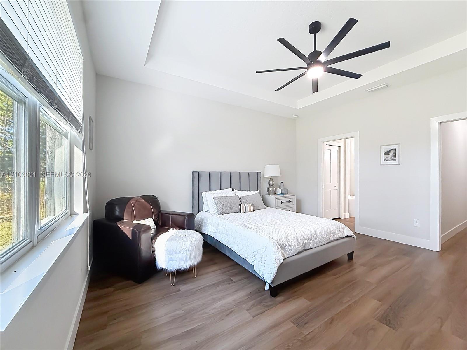 Bedroom featuring a tray ceiling, multi-blade ceiling fan, wood-finish flooring, and large windows with blinds