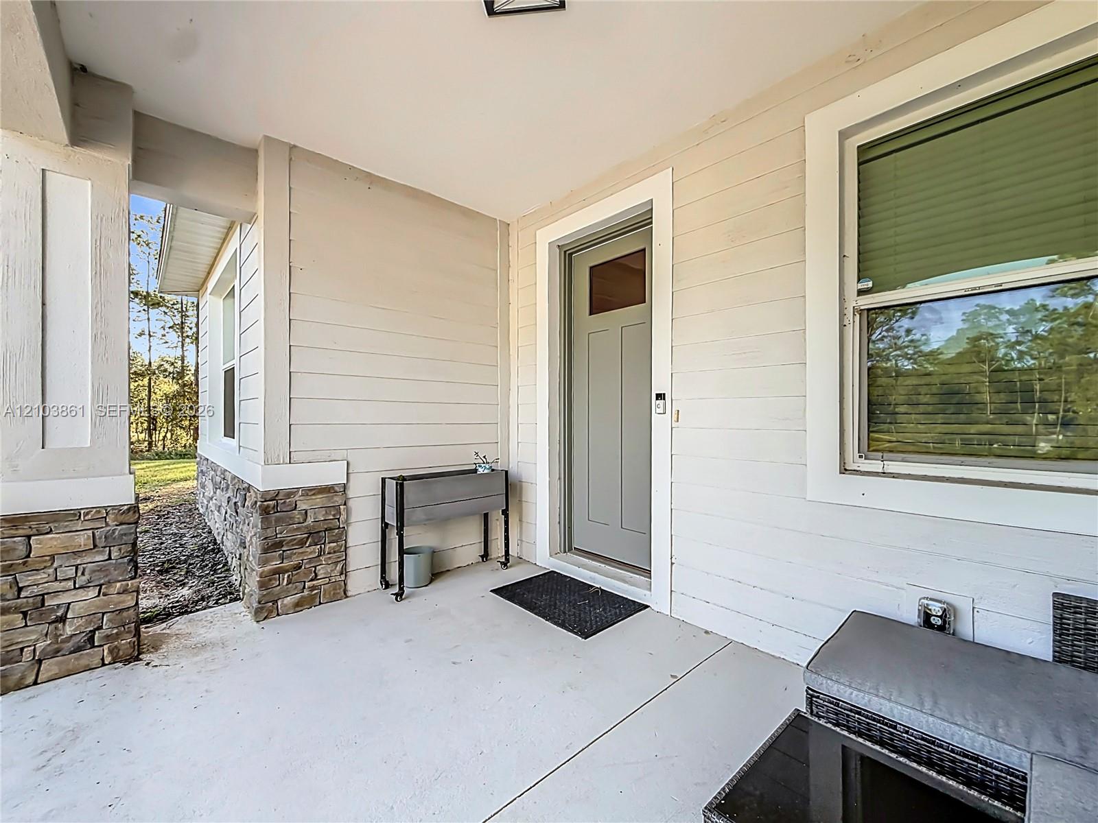 Covered front porch featuring horizontal lap siding, stacked stone base detailing, and a solid-core front door with an upper glass insert