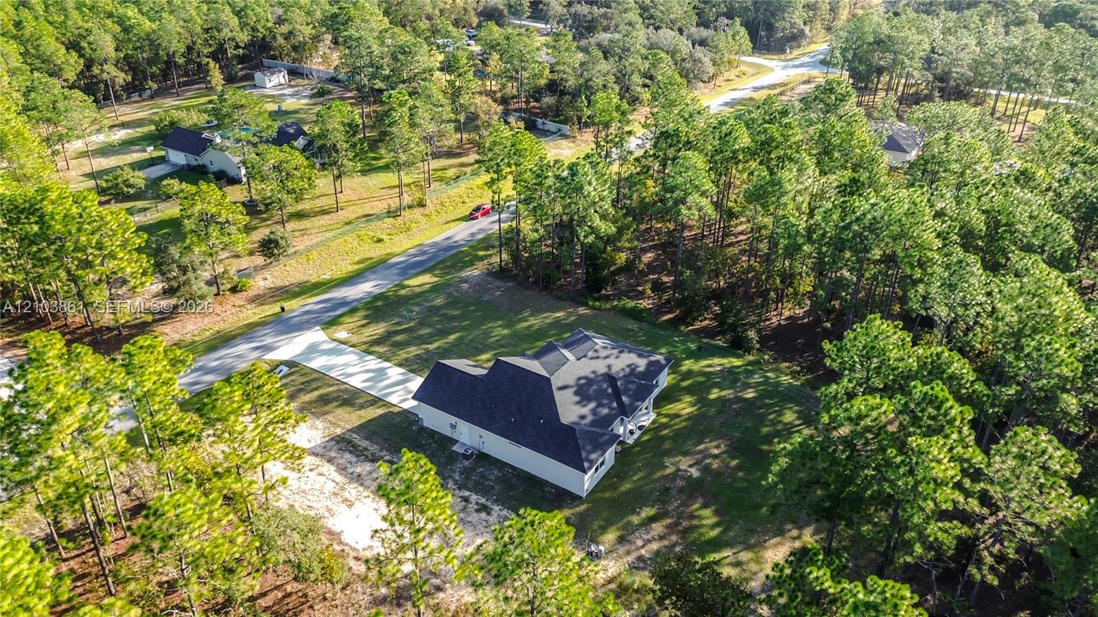 Aerial perspective featuring a single-story residence with a multi-gabled roof, concrete driveway, and surrounding wooded acreage