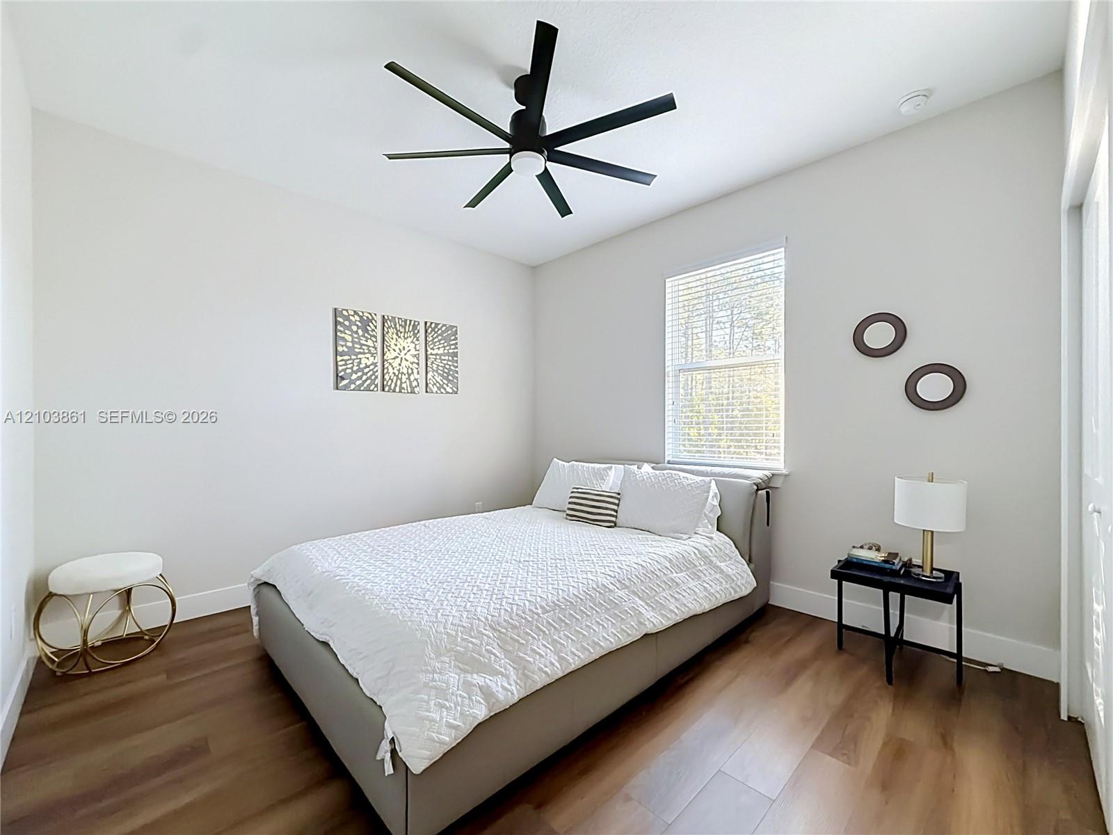 Wood-finish flooring, multi-blade matte black ceiling fan, and window with integrated blinds