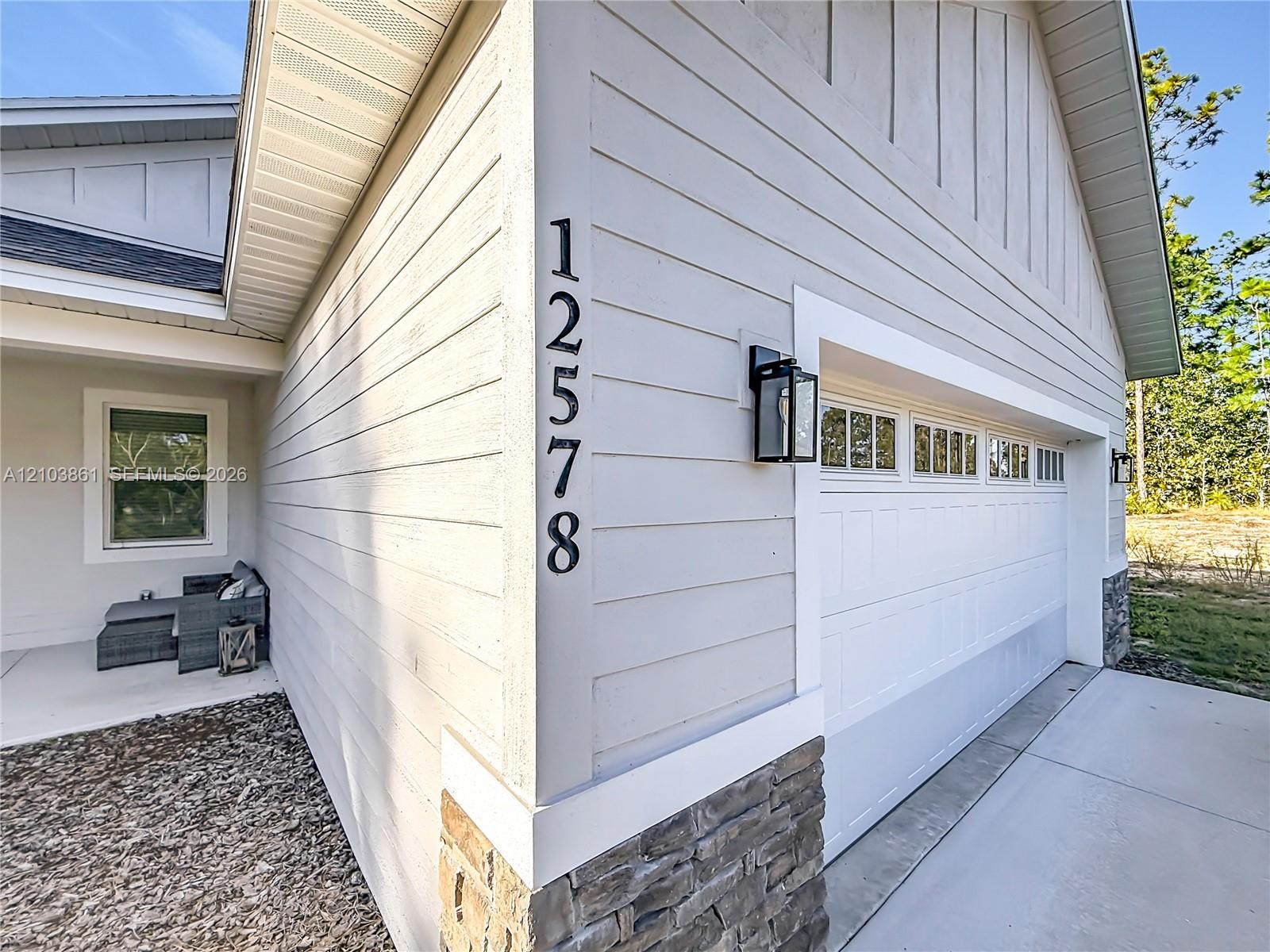 Exterior facade featuring horizontal lap siding, stone veneer accents, vertical paneling in the gable, and a paneled garage door with window inserts
