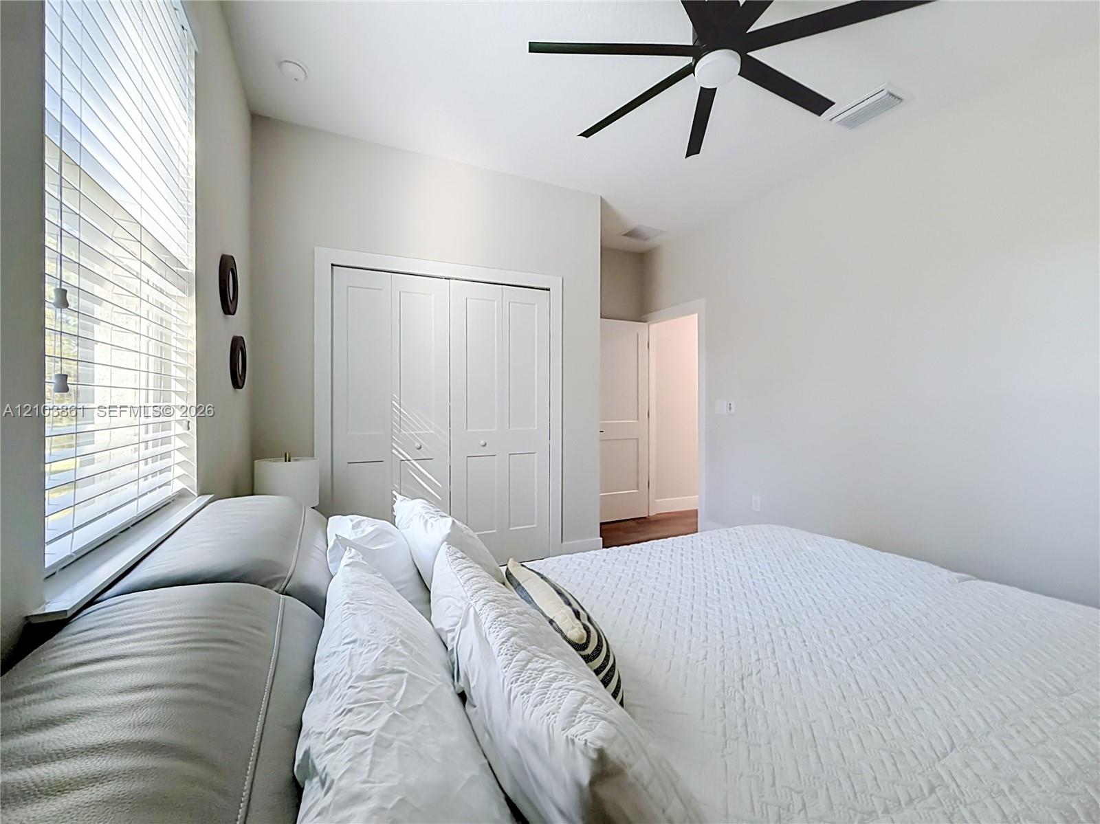 Neutral interior featuring high ceilings, a multi-blade matte black ceiling fan, white paneled closet doors, and horizontal slat window blinds
