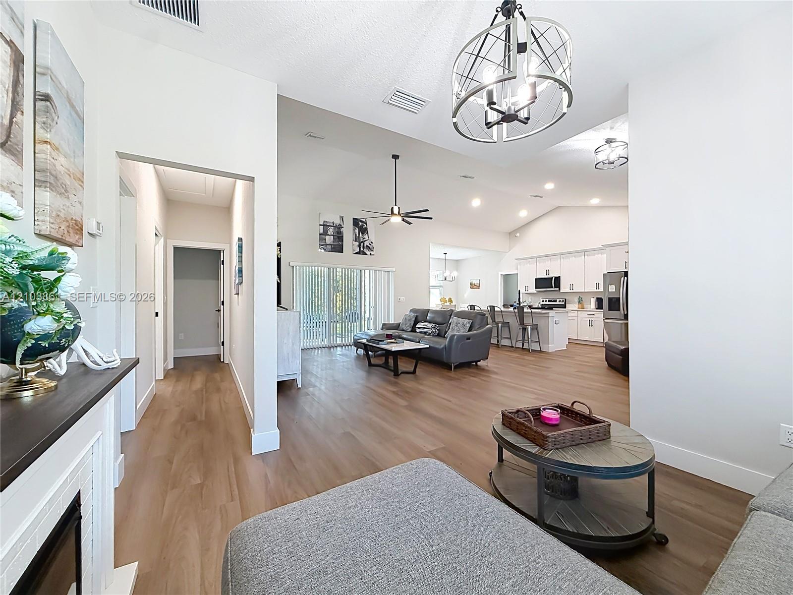 Open-concept interior featuring wood-finish flooring, vaulted ceilings, a metallic cage-style chandelier, white cabinetry, and recessed lighting