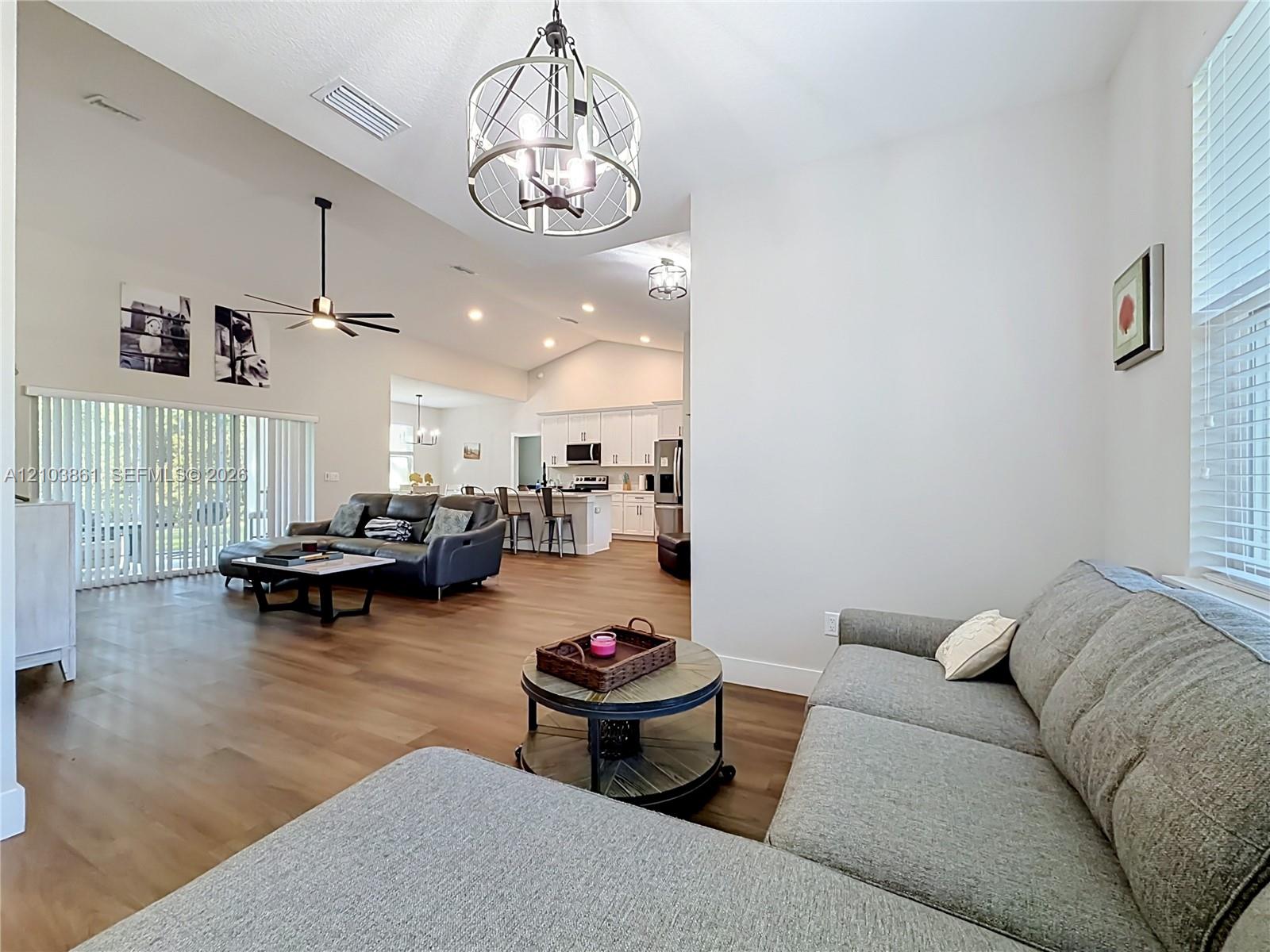 Vaulted ceilings, wood-finish flooring, metal drum pendant lighting, recessed lighting, and white cabinetry