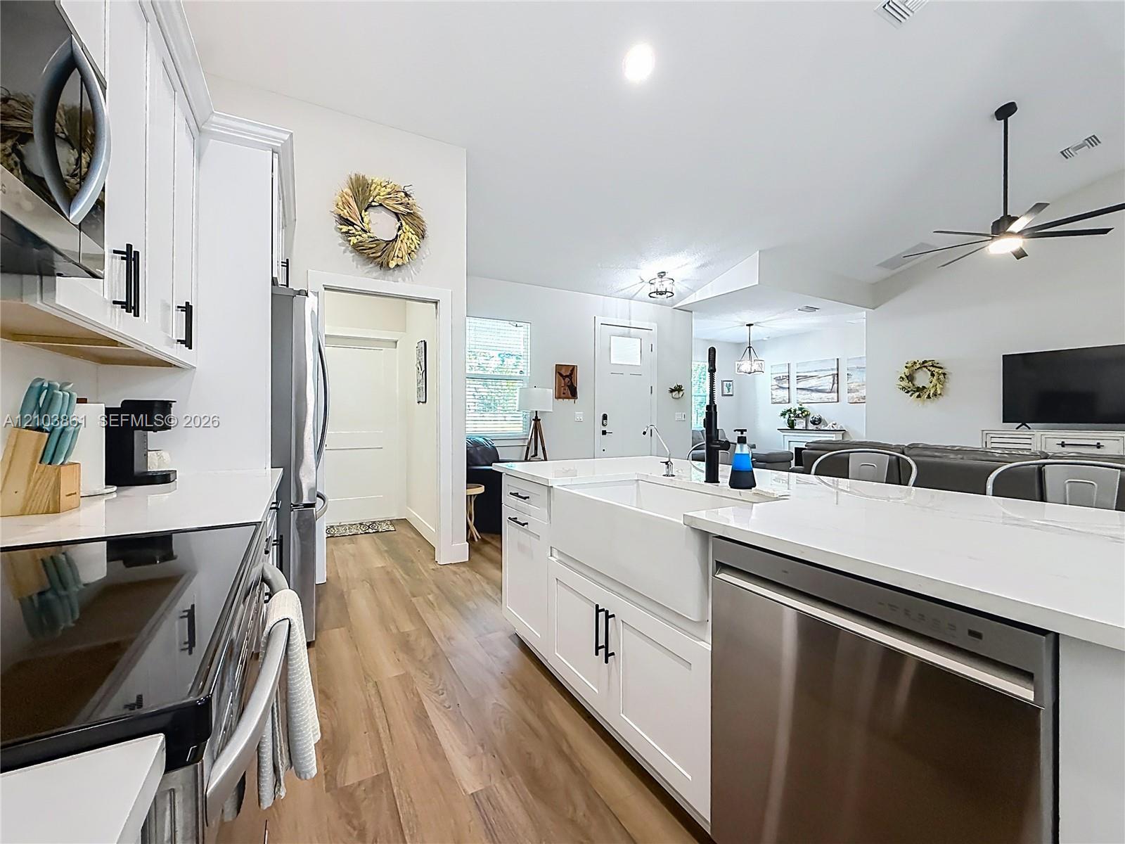Kitchen featuring white cabinetry, quartz countertops, a farmhouse-style apron sink, matte black hardware, and wood-finish flooring