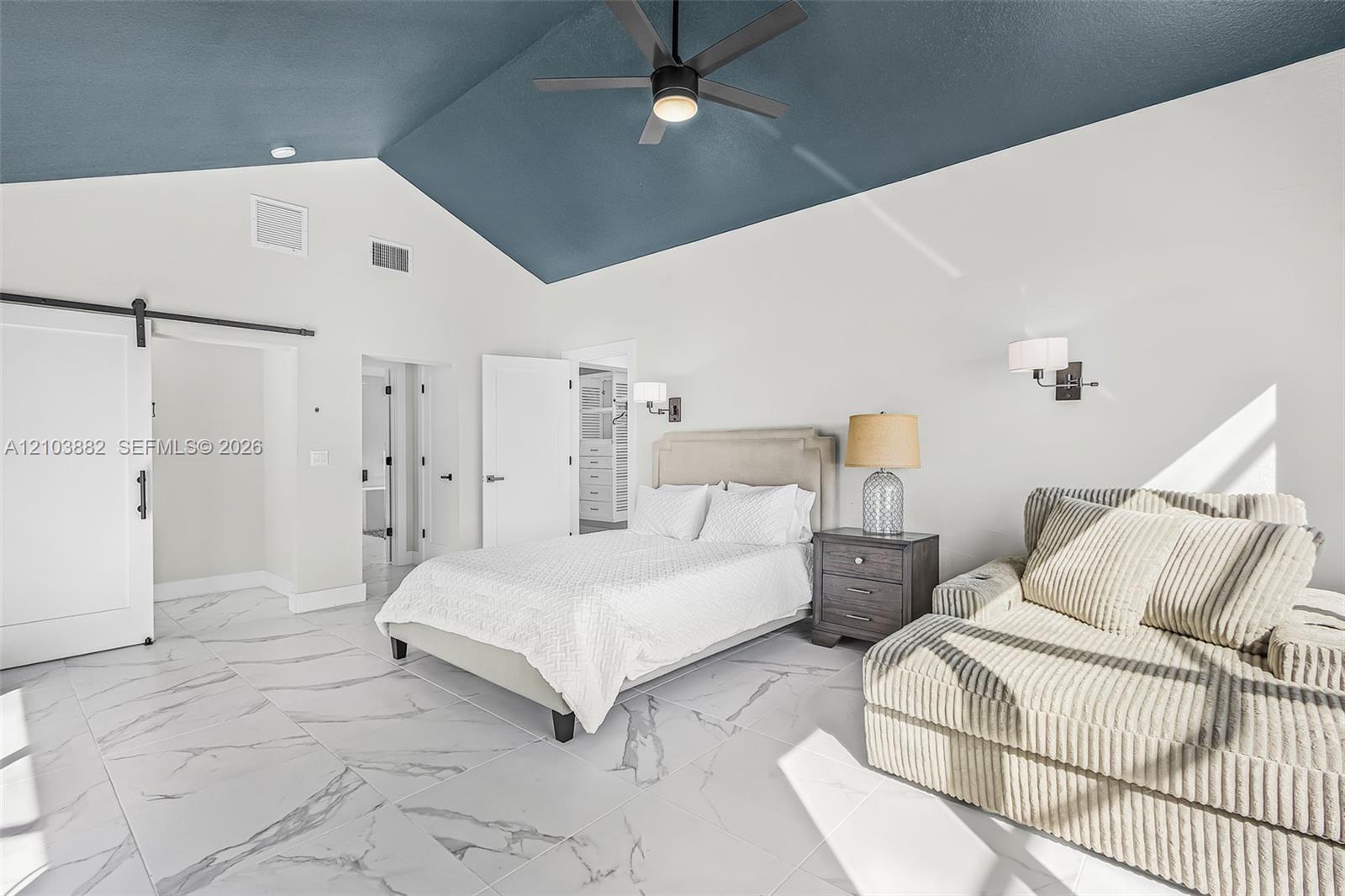 Vaulted ceiling with deep blue accent, large-format stone-finish tile flooring, sliding barn door, and wall-mounted light fixtures