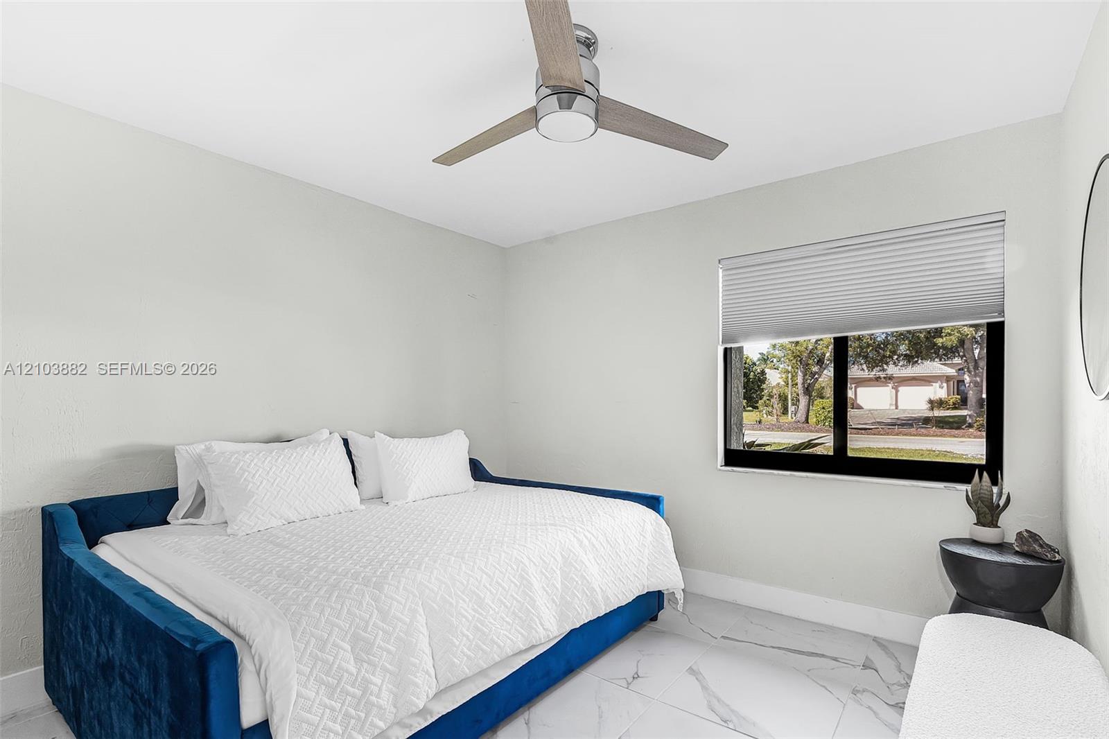 Neutral-toned room featuring large-format tile flooring with marble-style veining, a modern three-blade ceiling fan with an integrated light fixture, and a window equipped with horizontal cellular shades