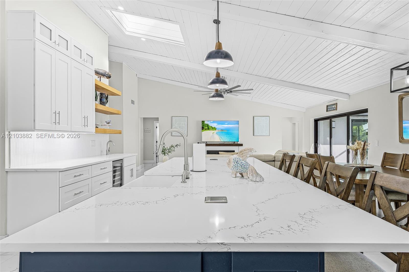 Kitchen featuring an oversized central island with stone-finish countertops, ceiling with exposed beams, skylights, matte black pendant lighting, and wood-finish cabinetry