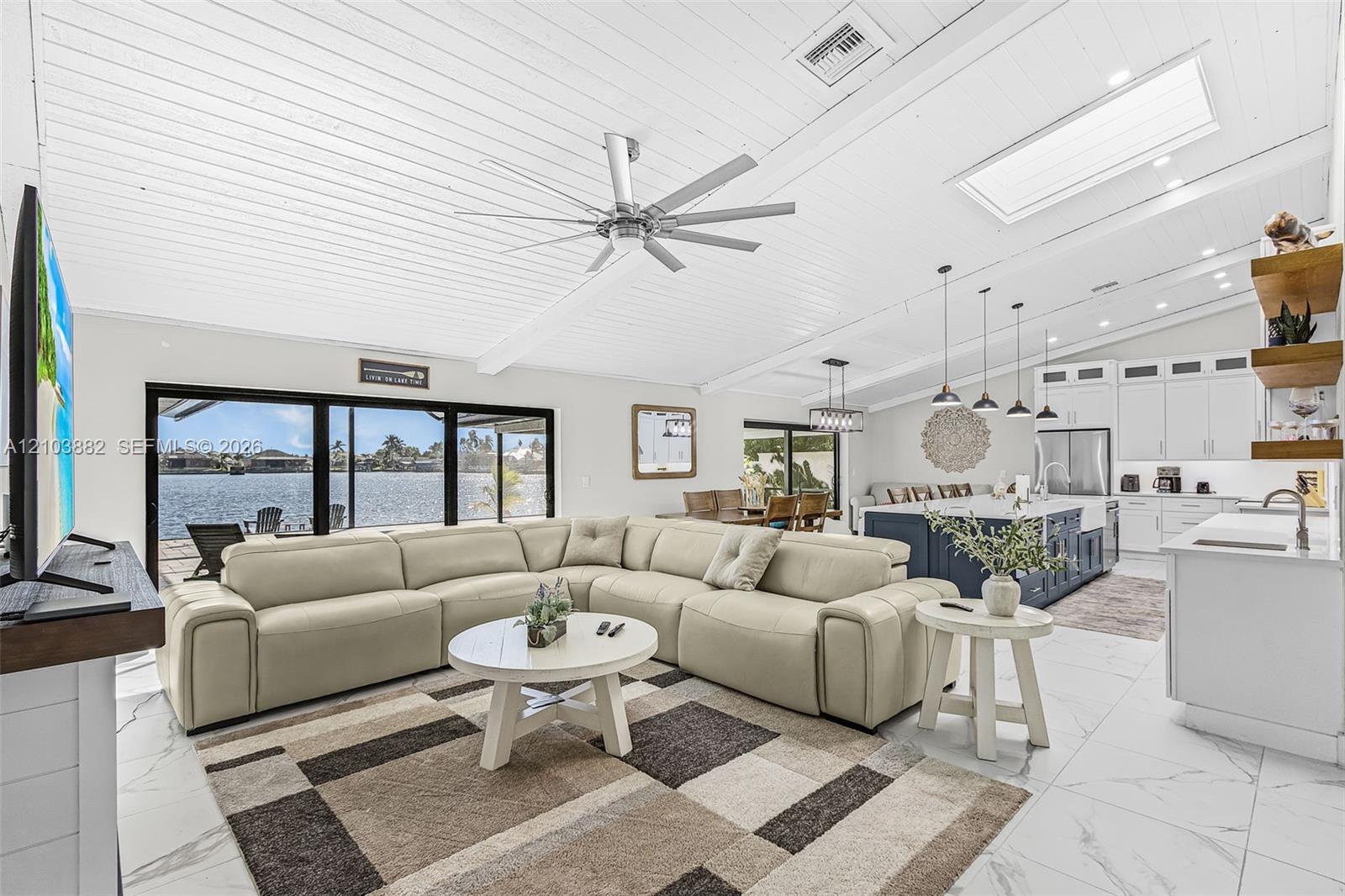 Vaulted tongue-and-groove ceiling with a central multi-blade ceiling fan, large-format tile flooring, skylight, and open-concept kitchen featuring an expansive center island
