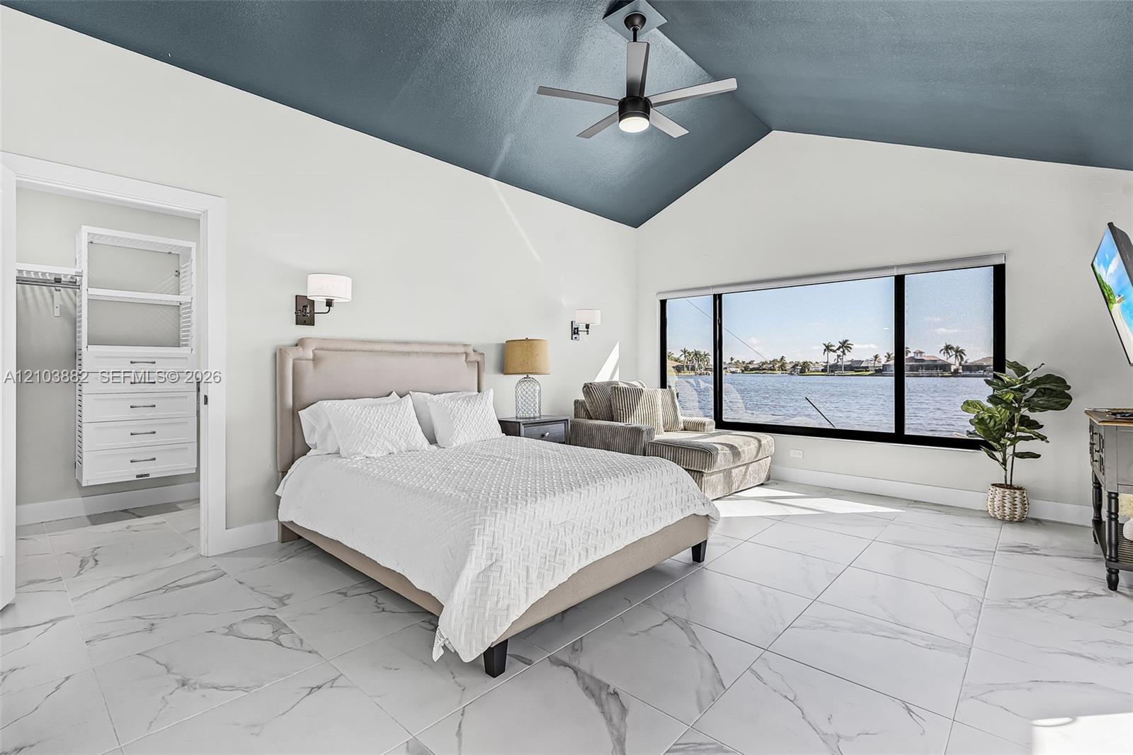 Vaulted ceiling with a matte-finish accent, large-format tile flooring with a stone pattern, floor-to-ceiling panoramic windows, built-in closet organization system, and wall-mounted light fixtures