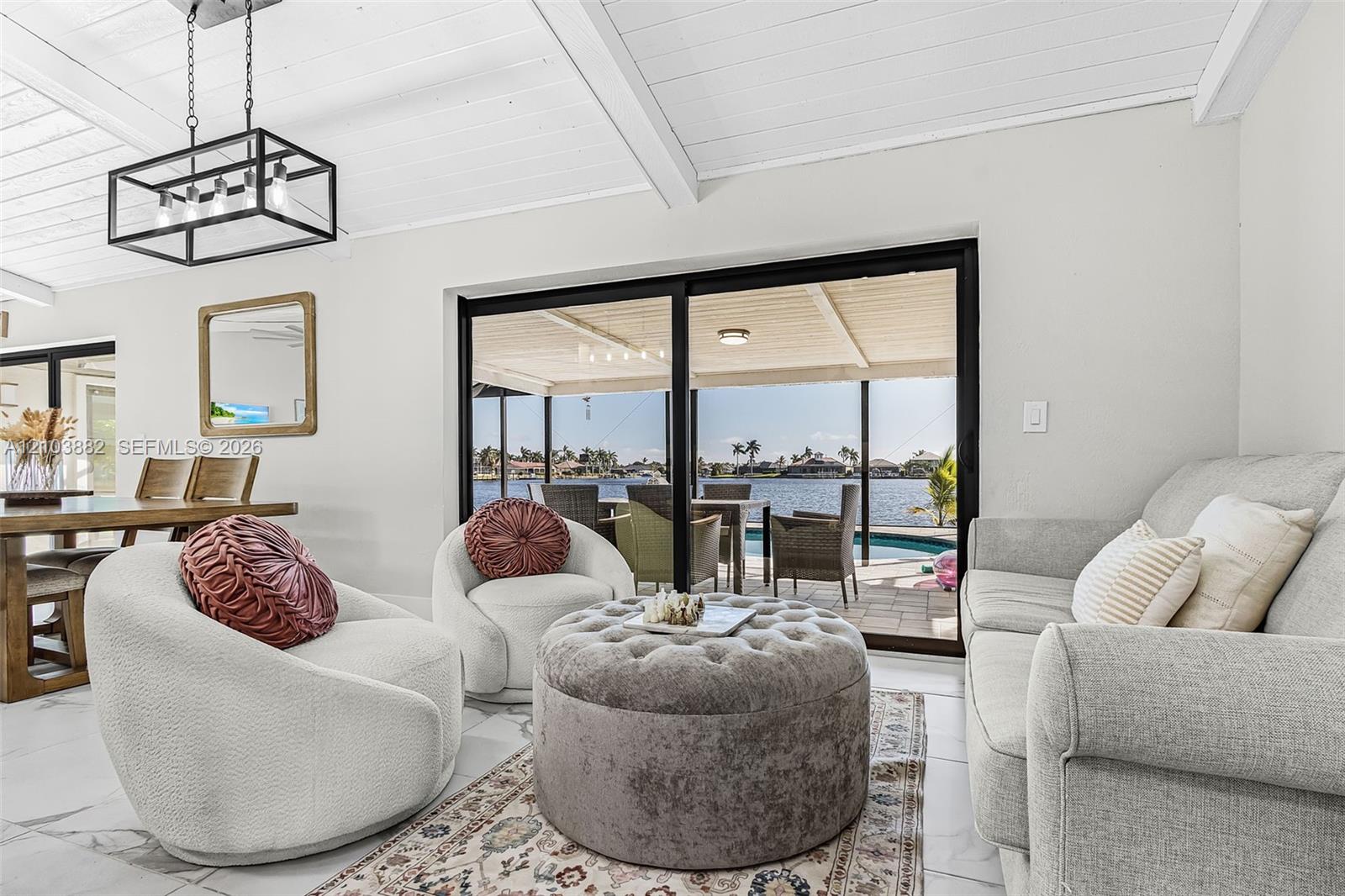 Living area featuring white vaulted ceilings with exposed beams, large-format tile flooring, a rectangular metal-frame pendant light, and oversized sliding glass doors