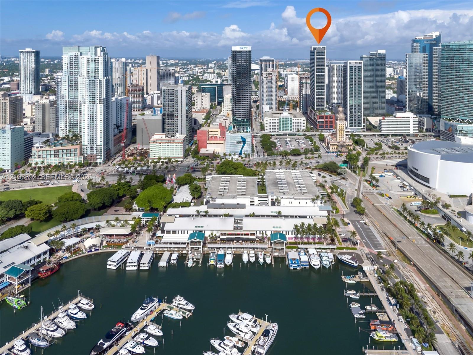 Aerial perspective of a high-rise tower featuring a prominent glass facade, situated within a metropolitan skyline near a waterfront marina