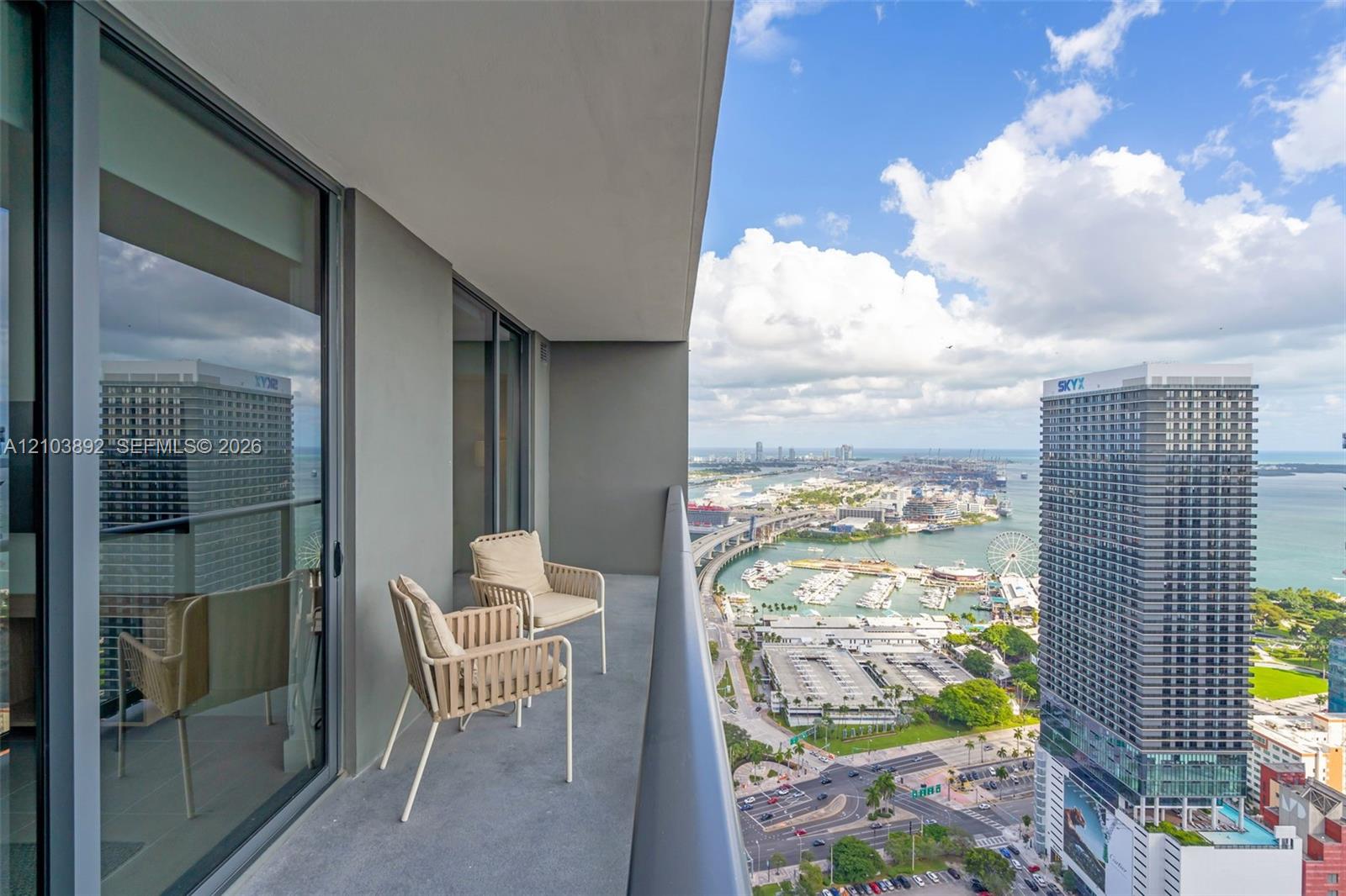 Covered balcony featuring concrete flooring, full-height sliding glass doors, and a metal railing