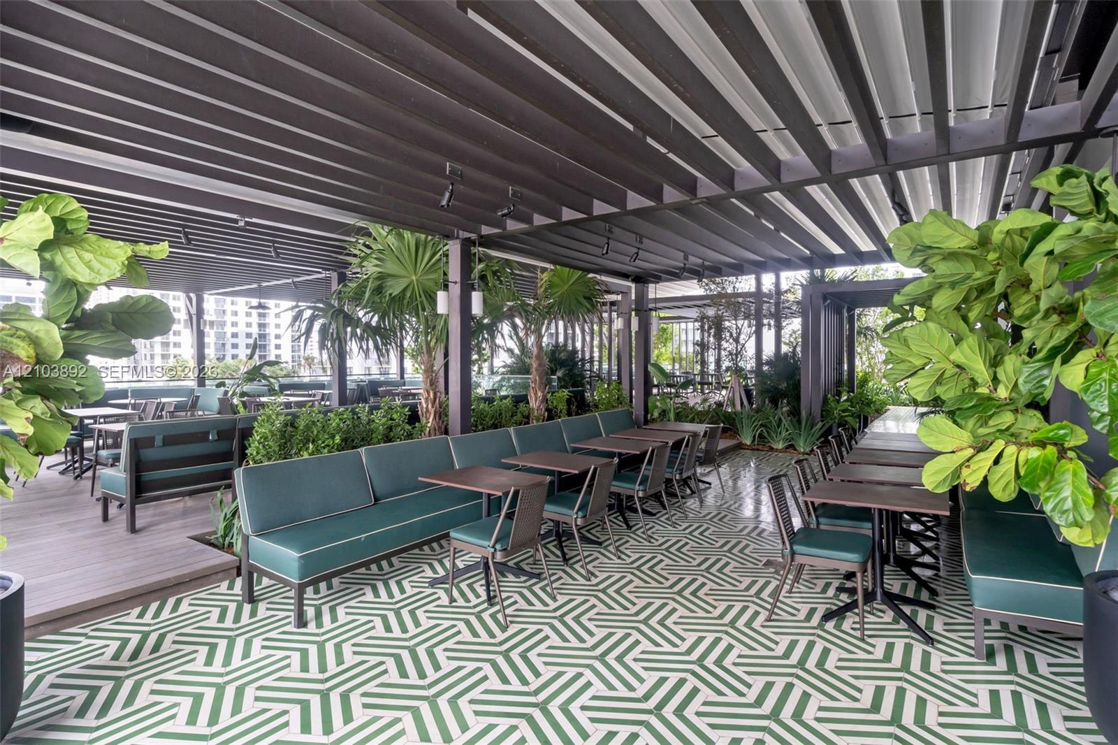 Covered outdoor terrace featuring a black metal louvered pergola, geometric patterned tile flooring, wood-finish decking, integrated track lighting, and built-in perimeter planters