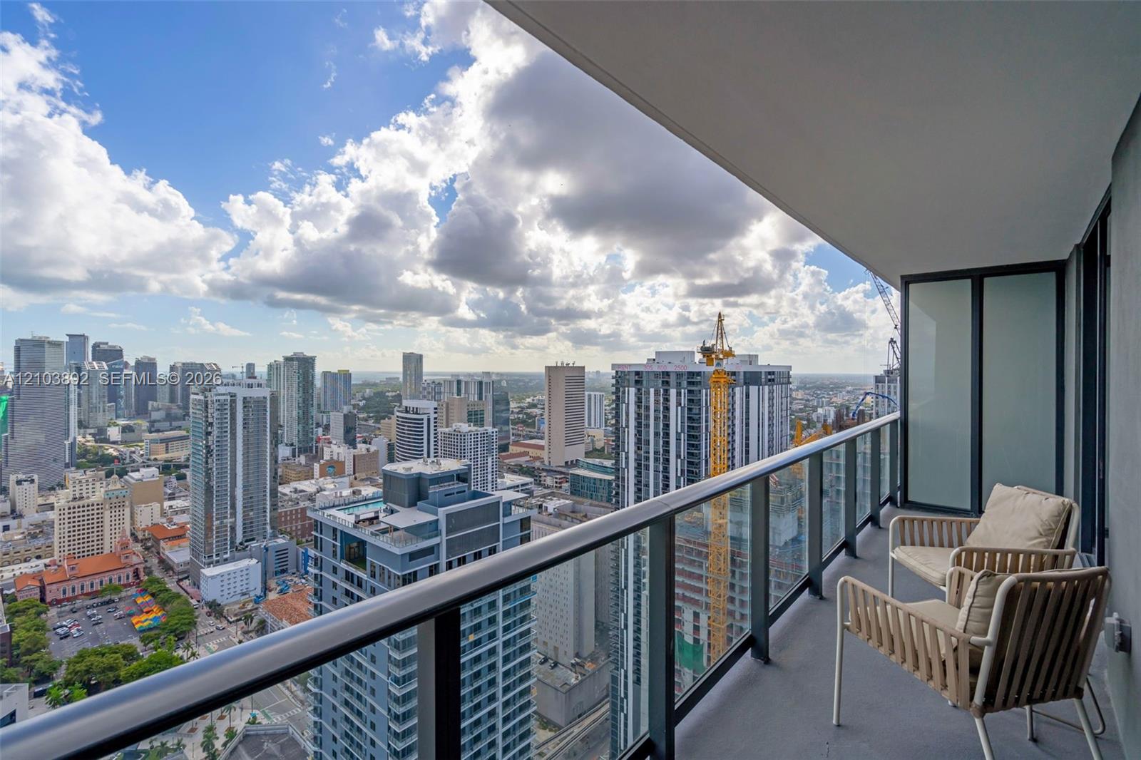 Private balcony with a metal and glass railing, concrete flooring, and panoramic urban skyline backdrop