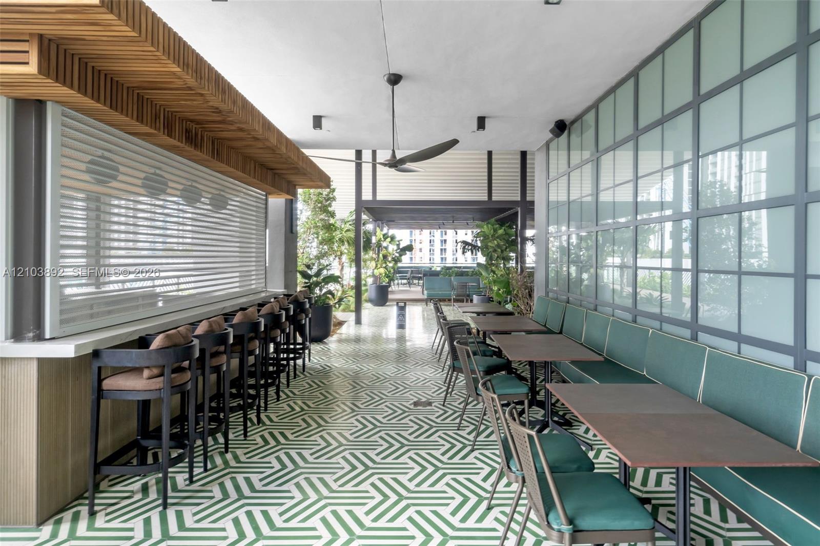 Outdoor covered lounge area featuring geometric patterned tile flooring, a built-in bar with wood-slat soffit detail, and industrial-style metal-framed glass wall partitions