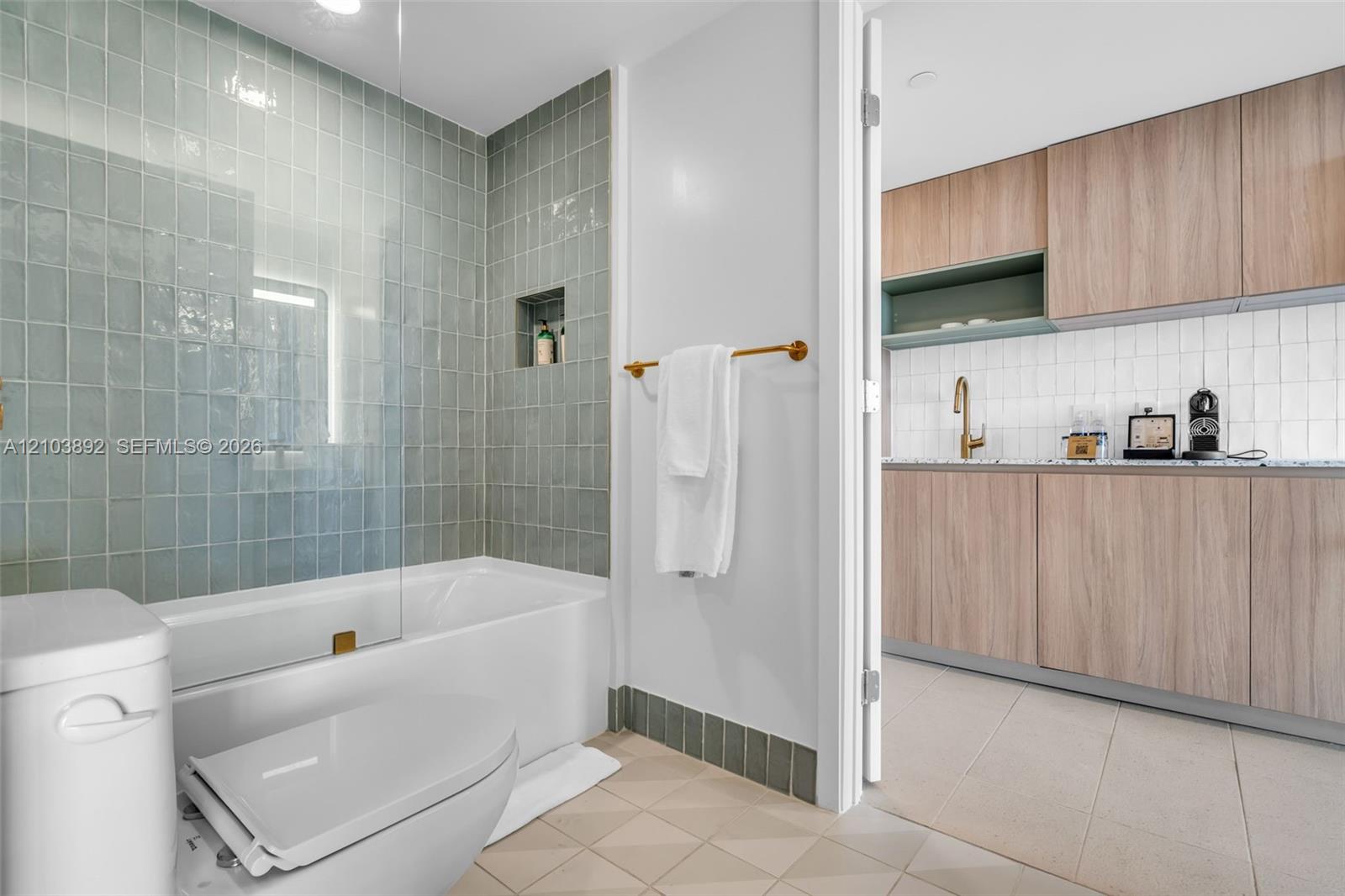 Bathroom featuring a built-in bathtub with floor-to-ceiling sage green tile surround, a glass shower partition, and a recessed wall niche
