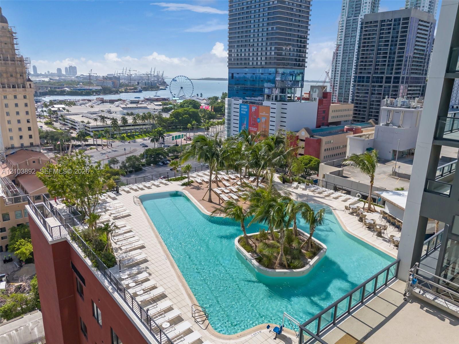 Rooftop pool featuring an island with palm trees, paved deck, and metal railings