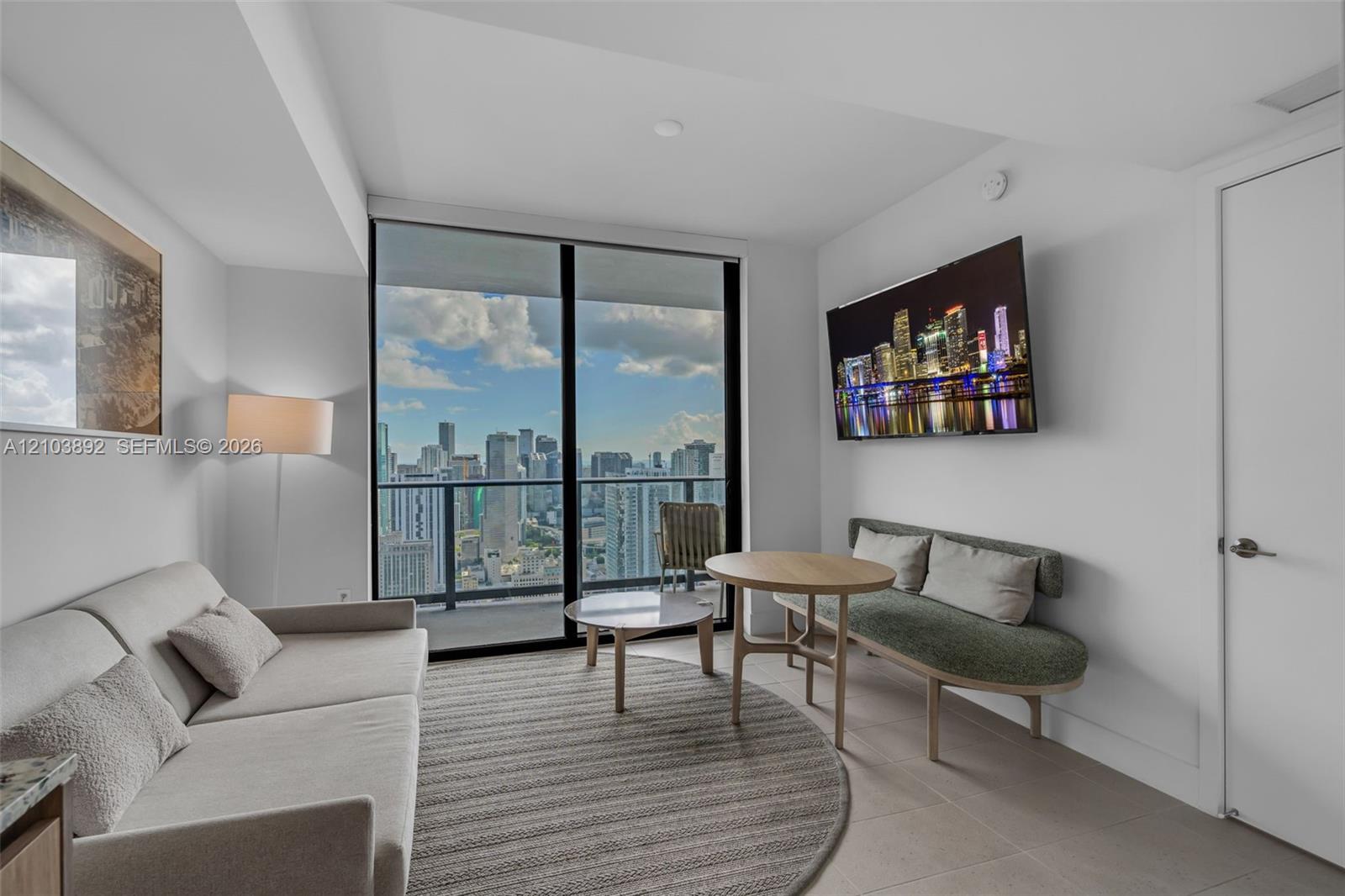 Floor-to-ceiling windows, private balcony, neutral tile flooring, and urban cityscape backdrop