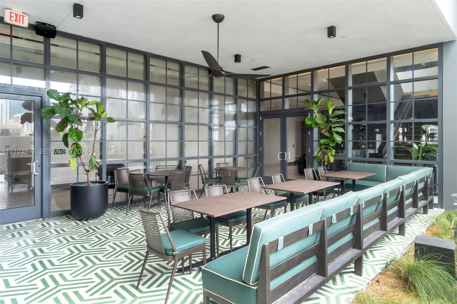 Covered patio featuring floor-to-ceiling metal-framed glass walls, geometric patterned tile flooring, and a ceiling-mounted fan