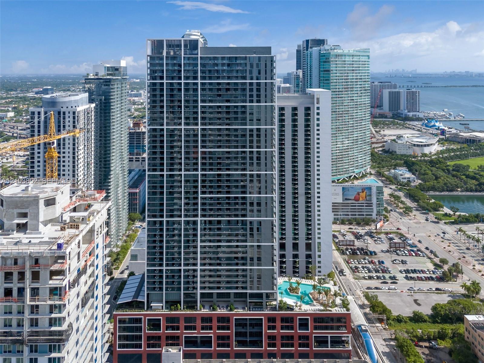 High-rise residential tower featuring a glass facade, private balconies, a podium-level outdoor swimming pool, and a multi-story red brick base