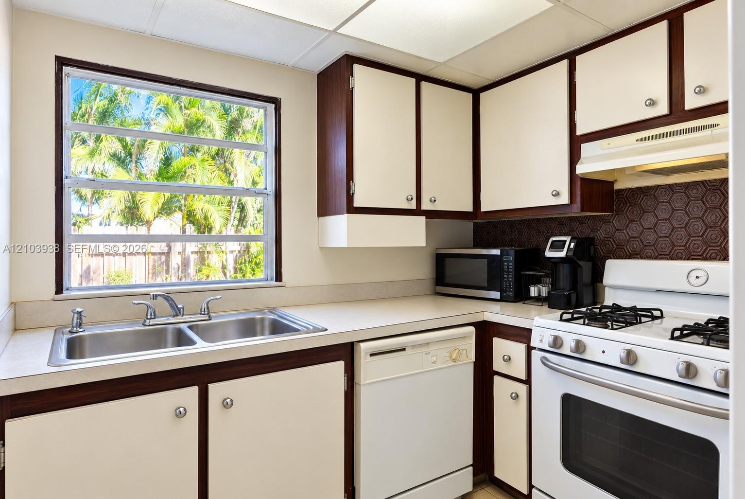 Kitchen featuring two-tone cabinetry, honeycomb patterned backsplash, double-basin stainless steel sink, and gas range