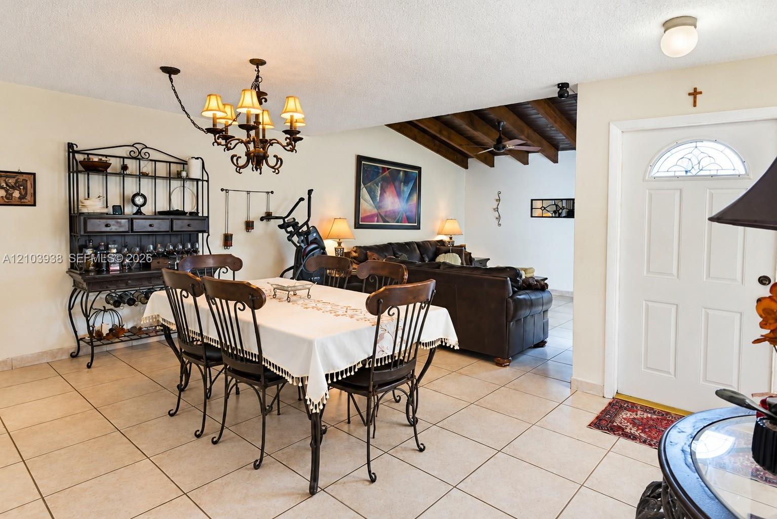 Ceramic tile flooring, exposed wood-beam ceiling, multi-light iron chandelier, and exterior entry door with an arched glass insert