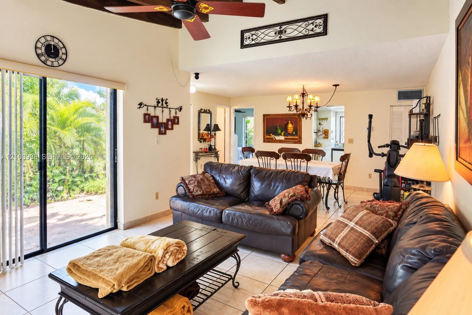 Open-concept interior featuring vaulted ceilings with exposed wood beams, ceiling fan, ceramic tile flooring, and large sliding glass doors