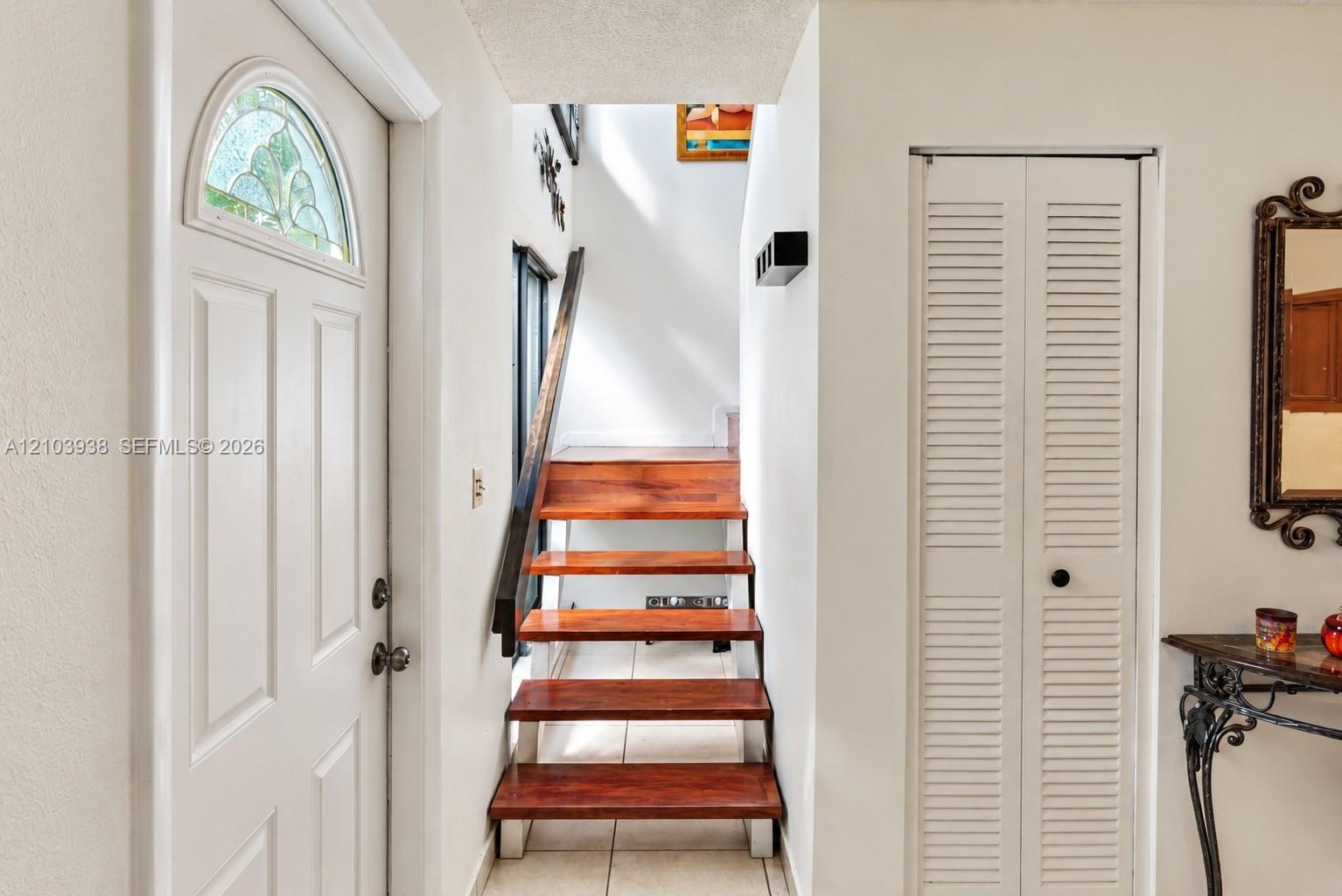Entryway featuring an arched front door with decorative glass inlay, open-riser staircase with wood-finish treads, and floor-to-ceiling louvered closet doors