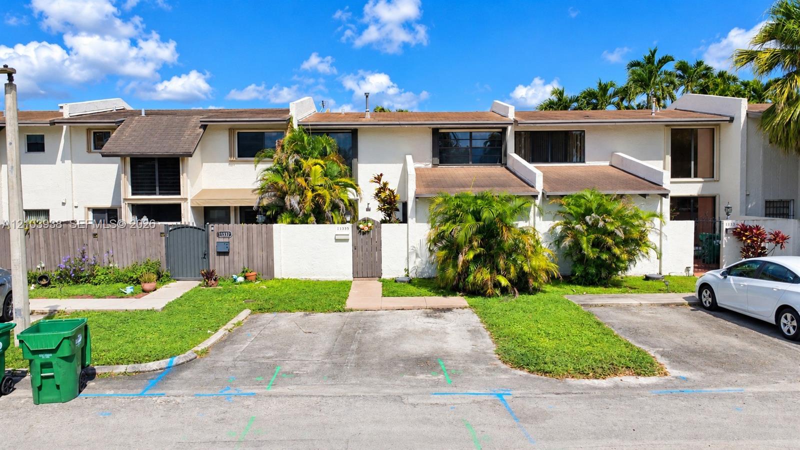 Exterior facade featuring multi-level townhouse architecture, white masonry walls, private fenced courtyard entryways, and dedicated asphalt parking