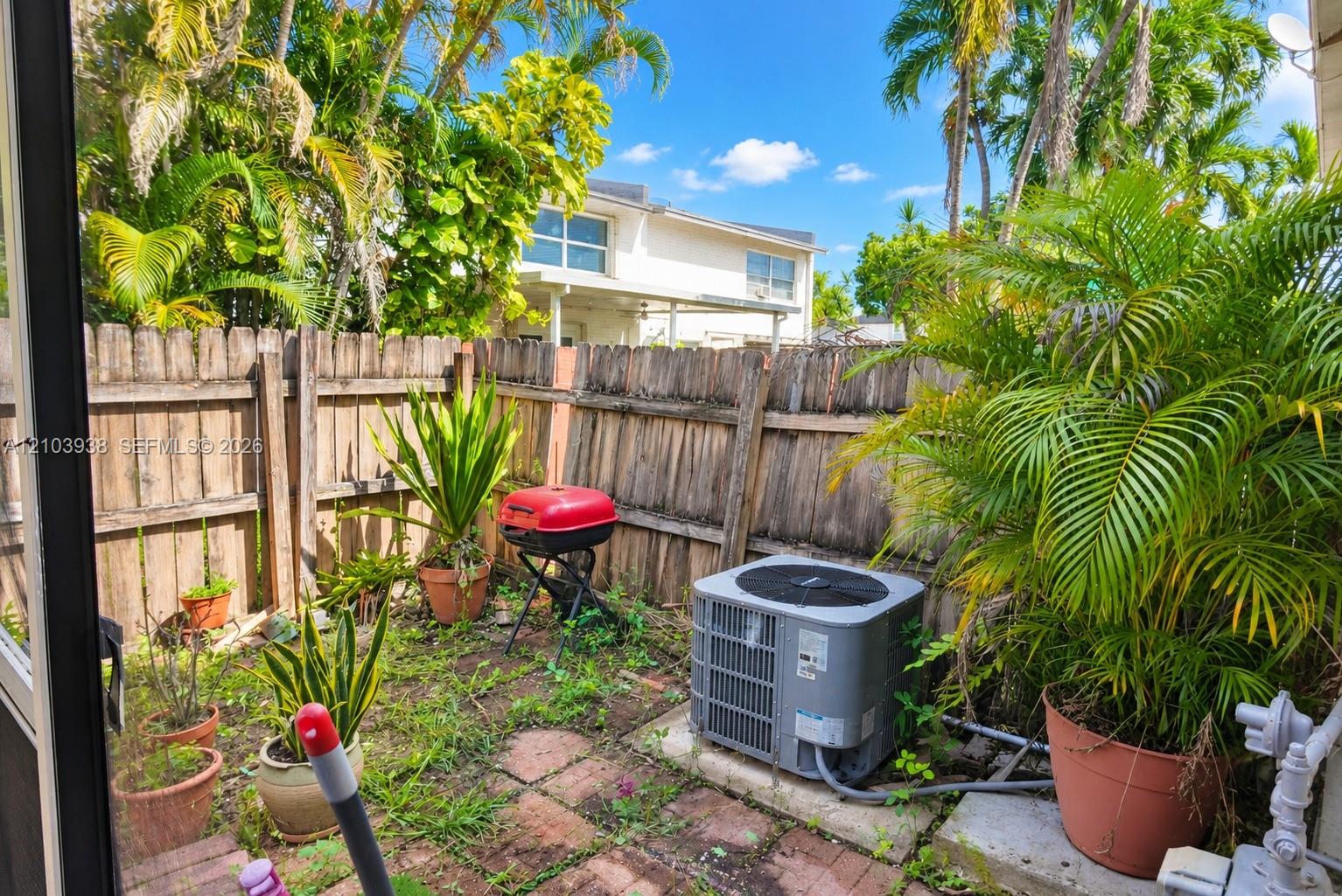 Private outdoor area featuring brick pavers, mature palm trees, and perimeter wood fencing