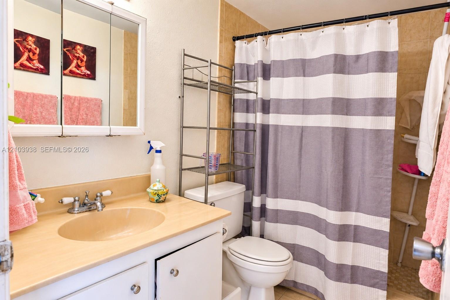 Bathroom featuring a vanity with integrated sink, dual-handle faucet, tri-fold medicine cabinet, and tile shower enclosure