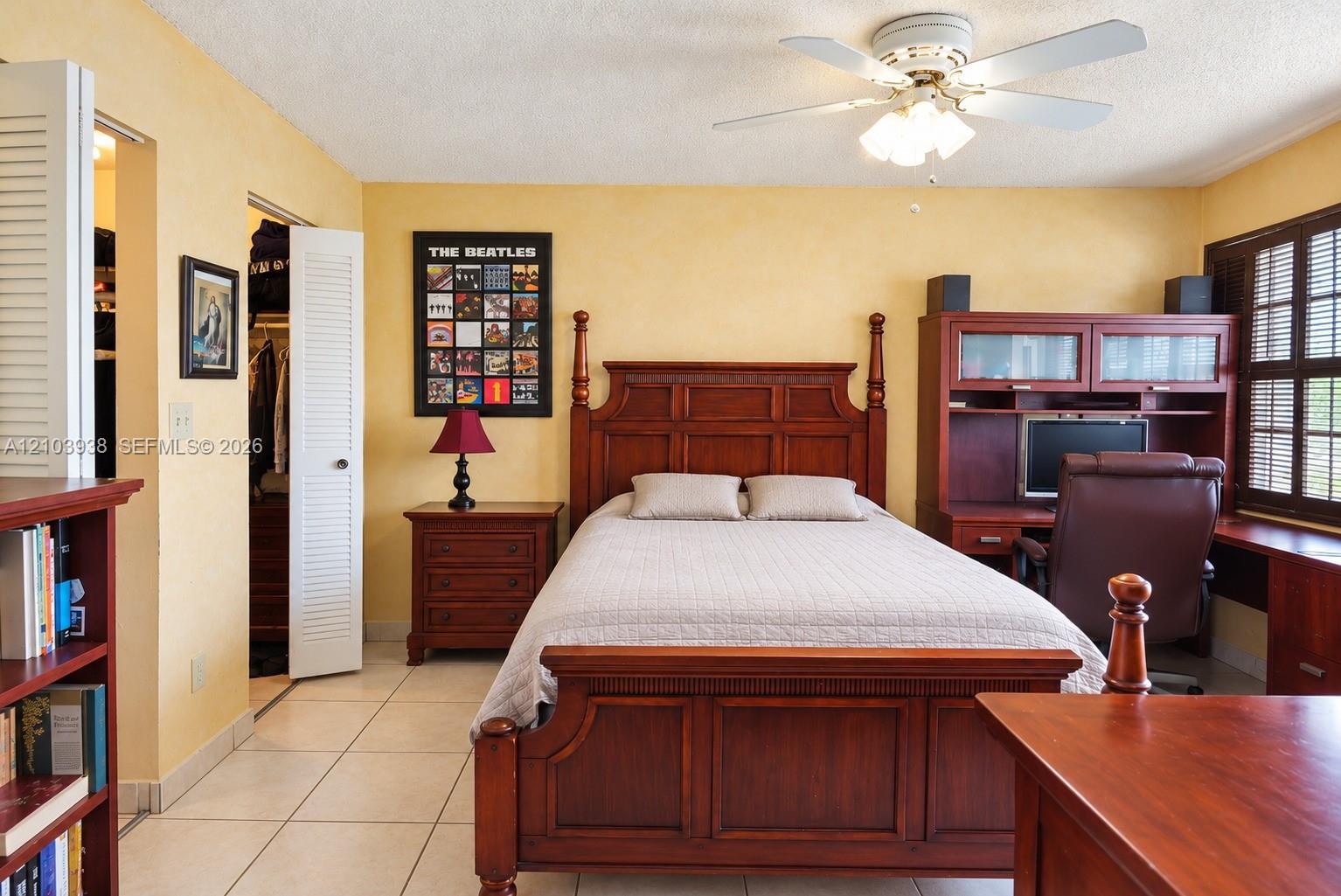 Room featuring tile flooring, ceiling fan with integrated lighting, louvered closet doors, and shutters