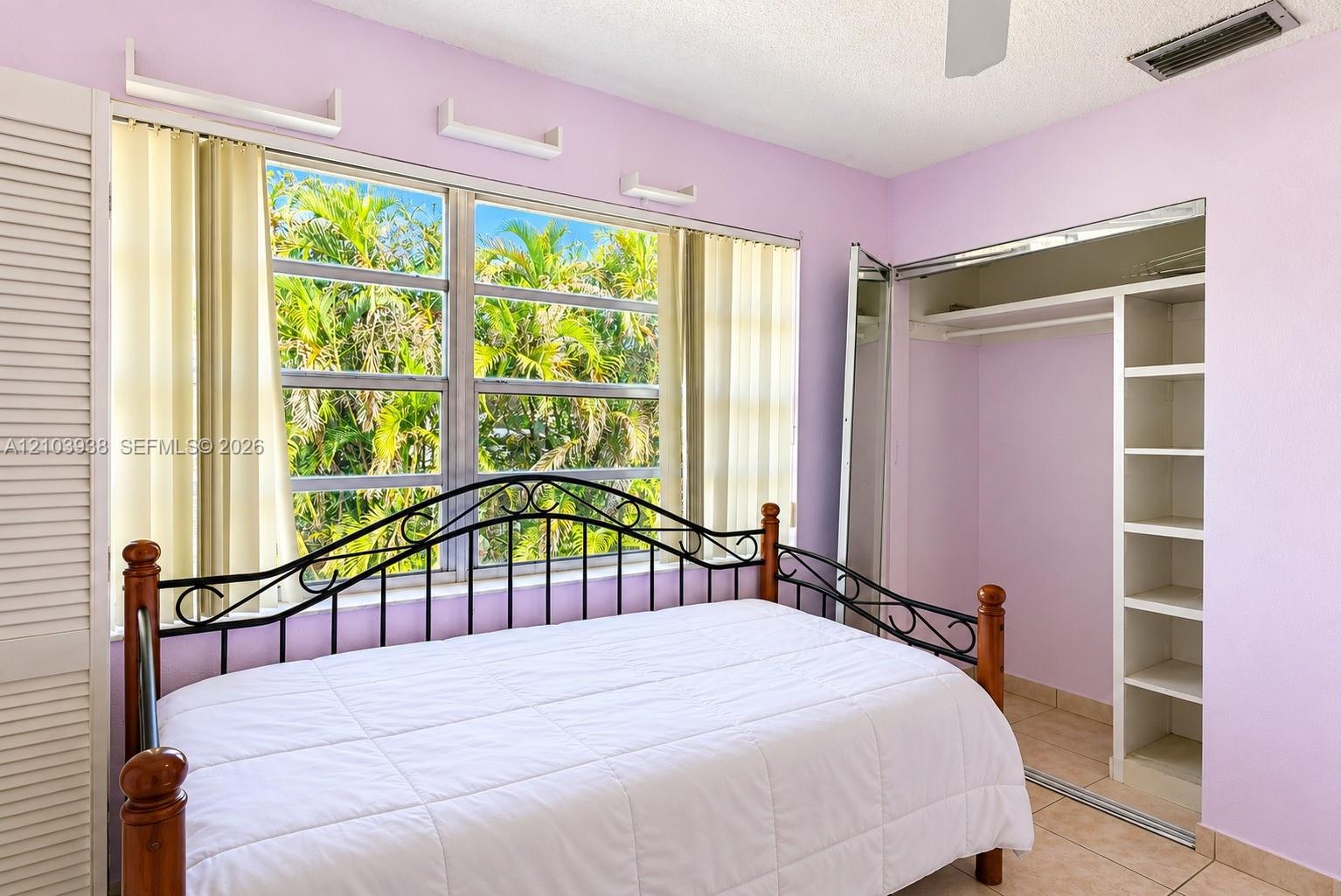 Large multi-pane window with natural exterior greenery, ceramic tile flooring, and built-in closet featuring shelving and hanging storage