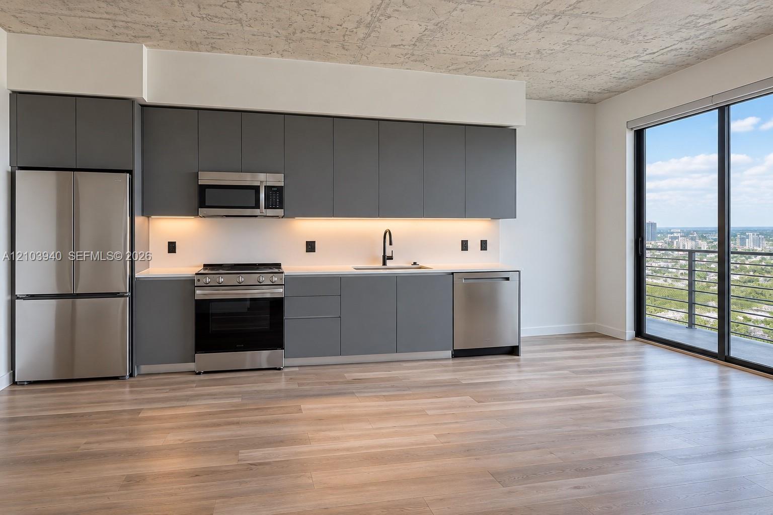 Modern kitchen featuring matte grey flat-panel cabinetry, stainless steel appliances, white stone-finish countertops, exposed concrete-texture ceiling, and floor-to-ceiling glass sliding doors Modern kitchen featuring matte grey flat-panel cabinetry, stainless steel appliances, white stone-finish countertops, exposed concrete-texture ceiling, and floor-to-ceiling glass sliding doors