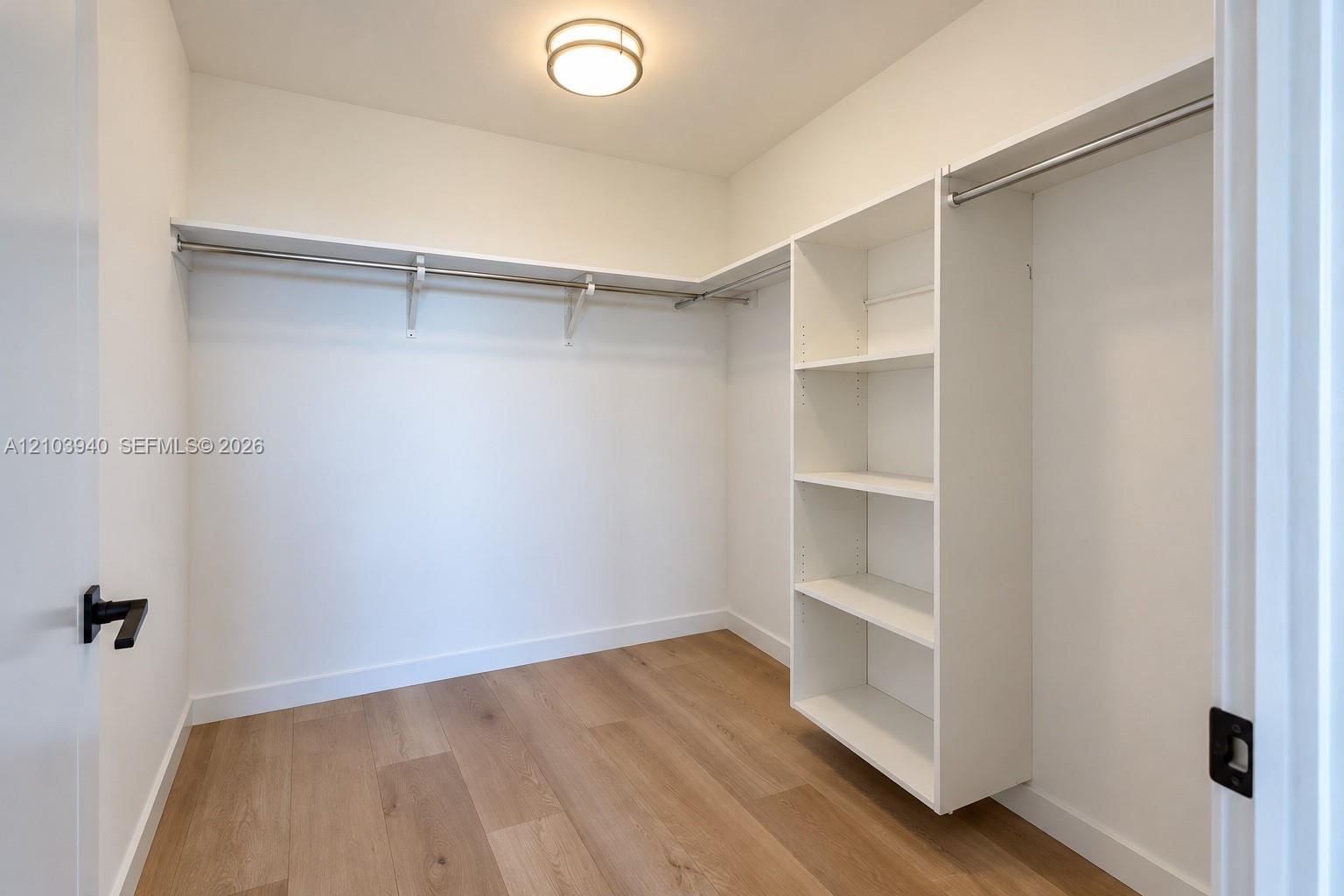 Walk-in closet featuring white built-in shelving, integrated metal hanging rods, wood-finish flooring, and a flush-mount ceiling light