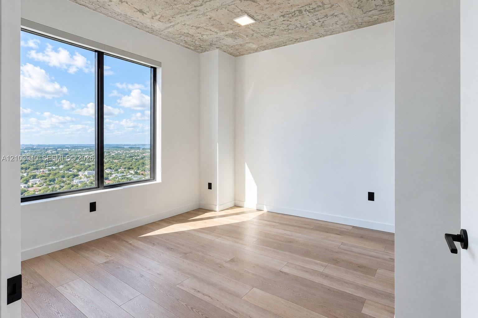 Room featuring wood-finish flooring, an exposed concrete ceiling, large-format window with dark trim, and white walls