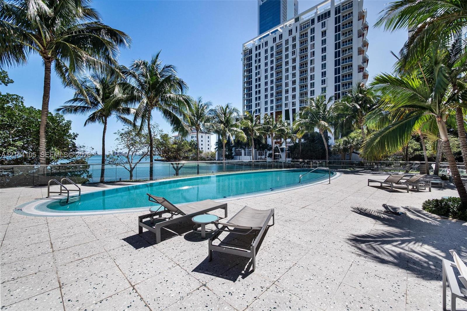 Resort-style pool area featuring a curved swimming pool, expansive paved deck, and mature palm trees