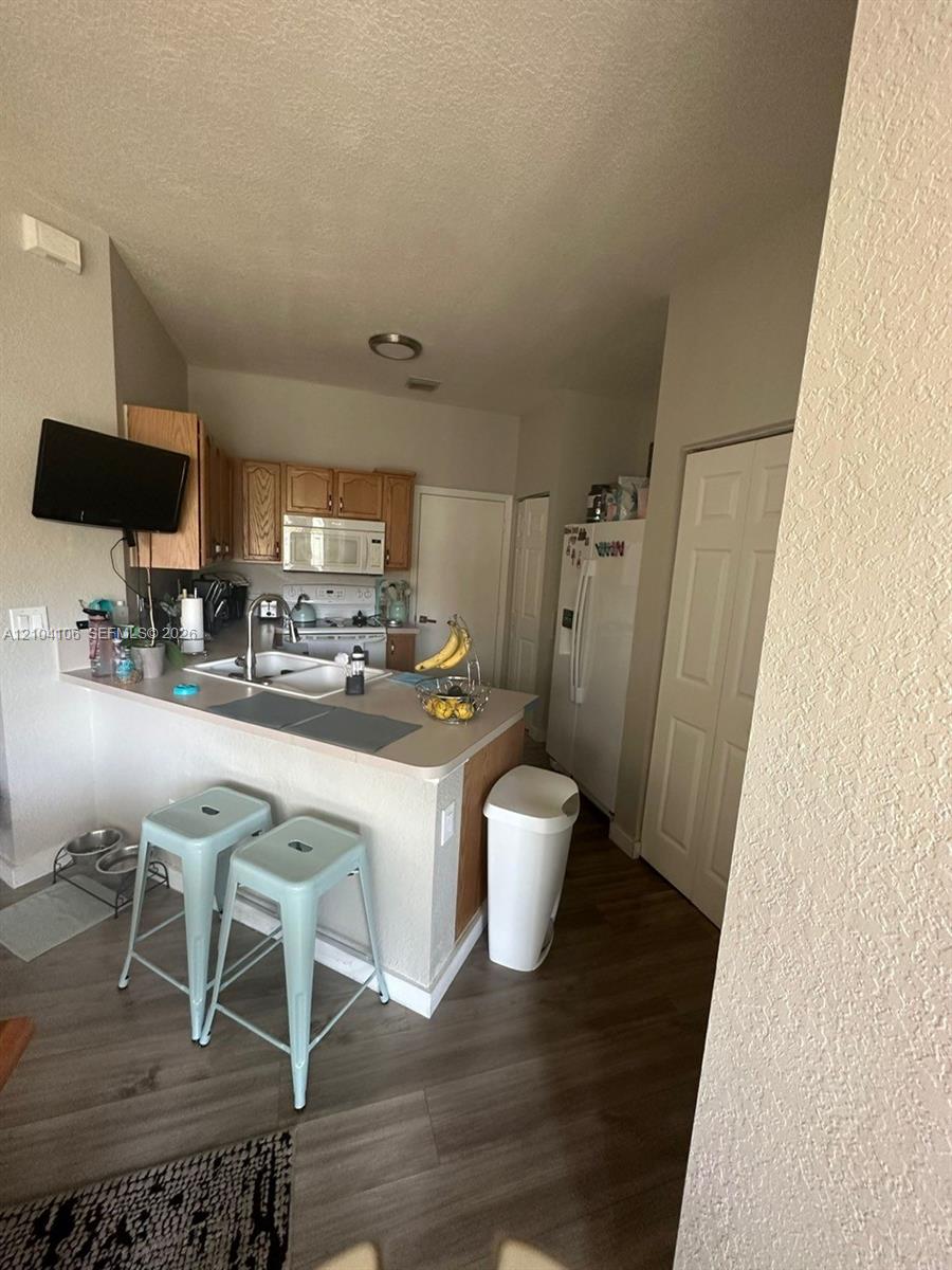 Kitchen featuring wood cabinetry, laminate countertops, a double-basin sink with a gooseneck faucet, an over-the-range microwave, and wood-finish flooring