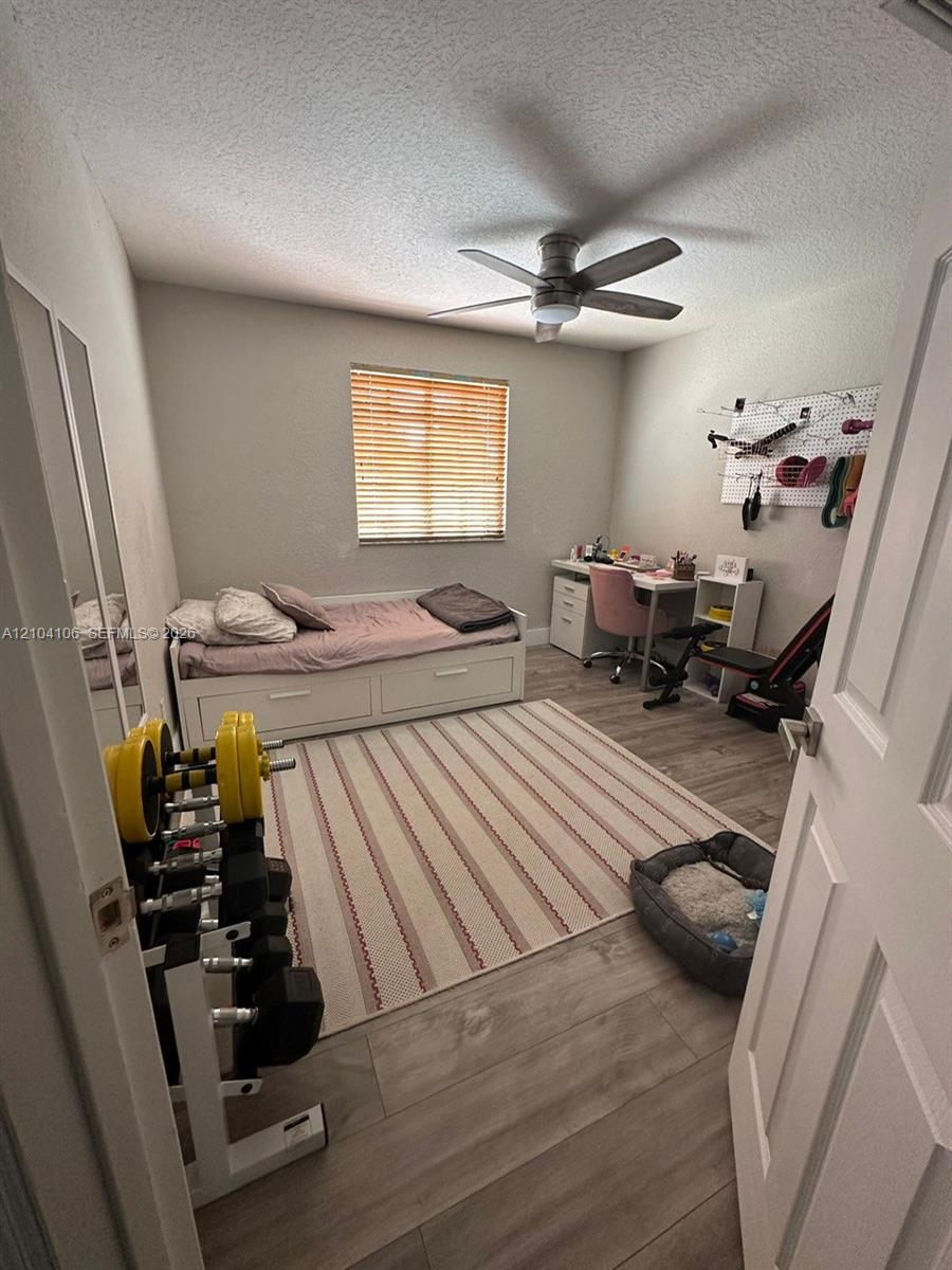 Room featuring wood-finish flooring, a ceiling fan with integrated lighting, and a window with blinds