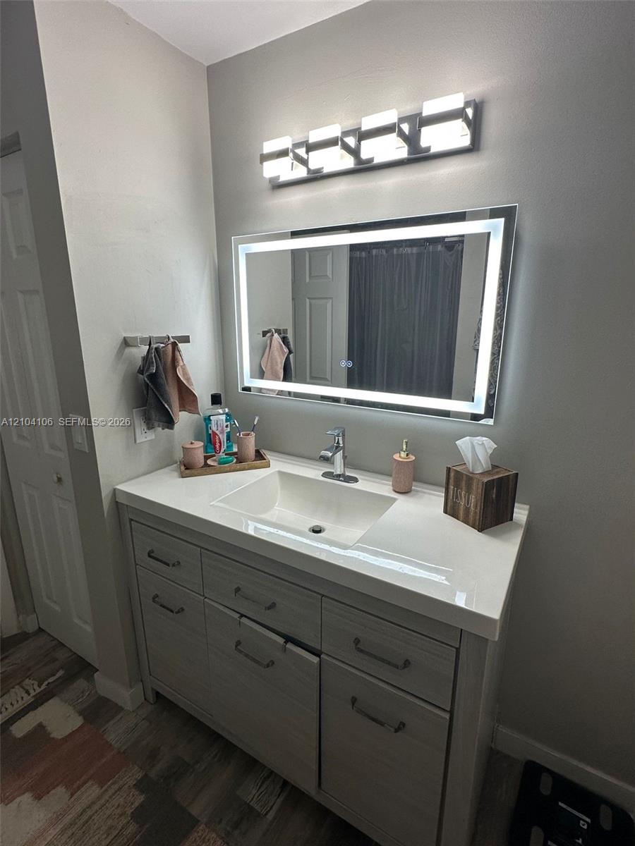 Modern vanity featuring a rectangular integrated sink, quartz countertop, wood-finish cabinetry, a rectangular LED-backlit mirror, and a four-light fixture