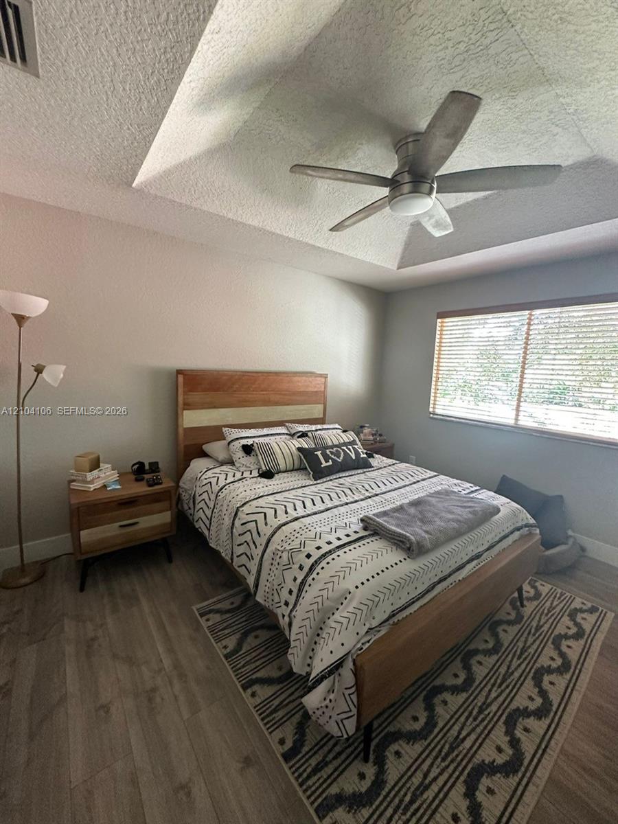 Tray ceiling with a central brushed-nickel ceiling fan, wood-finish flooring, and horizontal window blinds