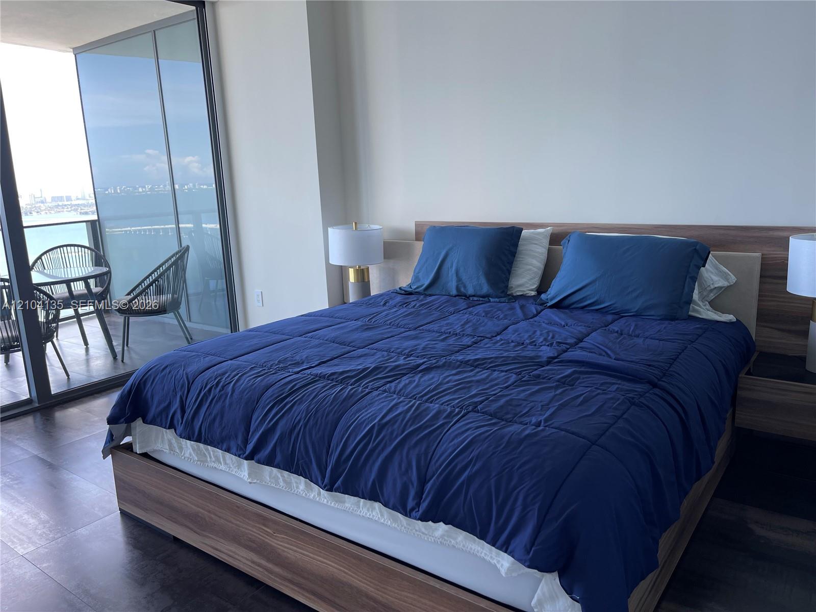 Floor-to-ceiling glass sliding doors, wood-finish platform bed frame with integrated headboard, and dark-toned flooring
