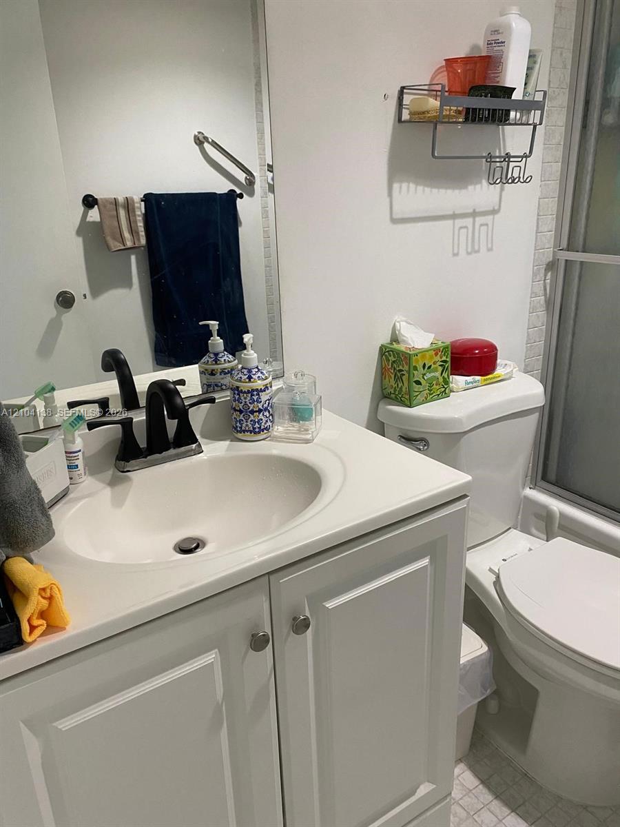 Bathroom vanity featuring a white cabinet, integrated sink, and matte black widespread faucet, accompanied by a wall-mounted mirror and shower enclosure