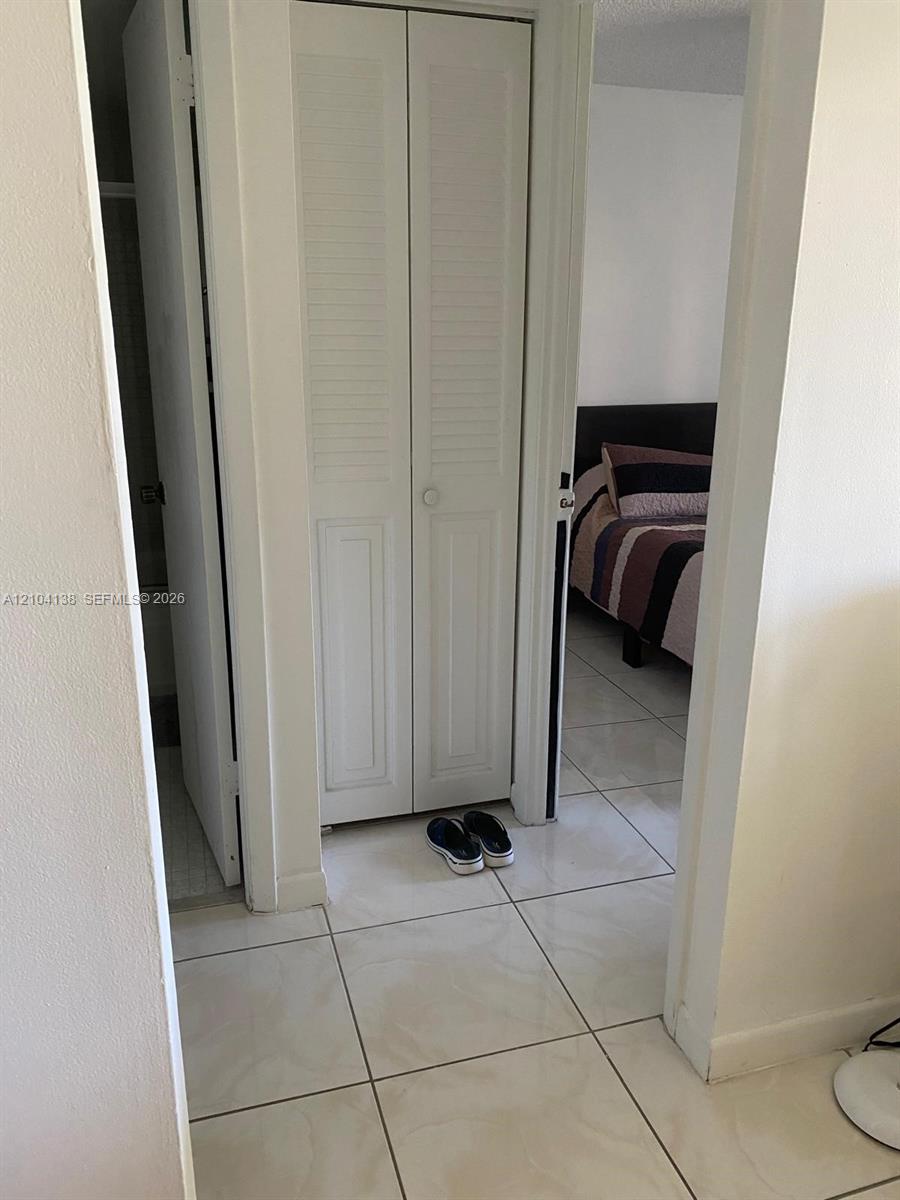White bi-fold louvered closet doors, neutral-toned square tile flooring, and standard interior door hardware